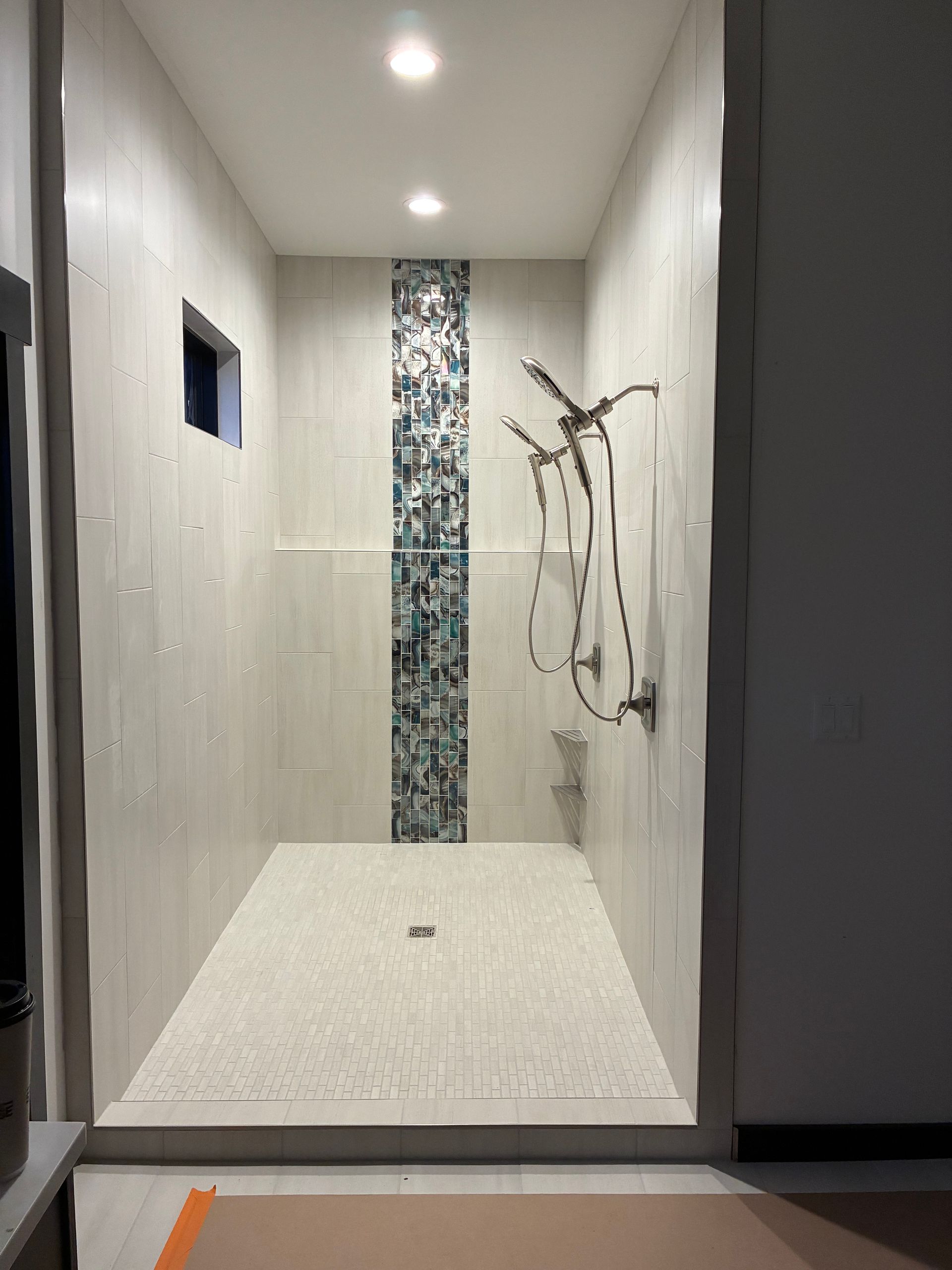 Modern shower with white tile, narrow mosaic accent strip, and rainfall showerhead in a tiled bathroom.