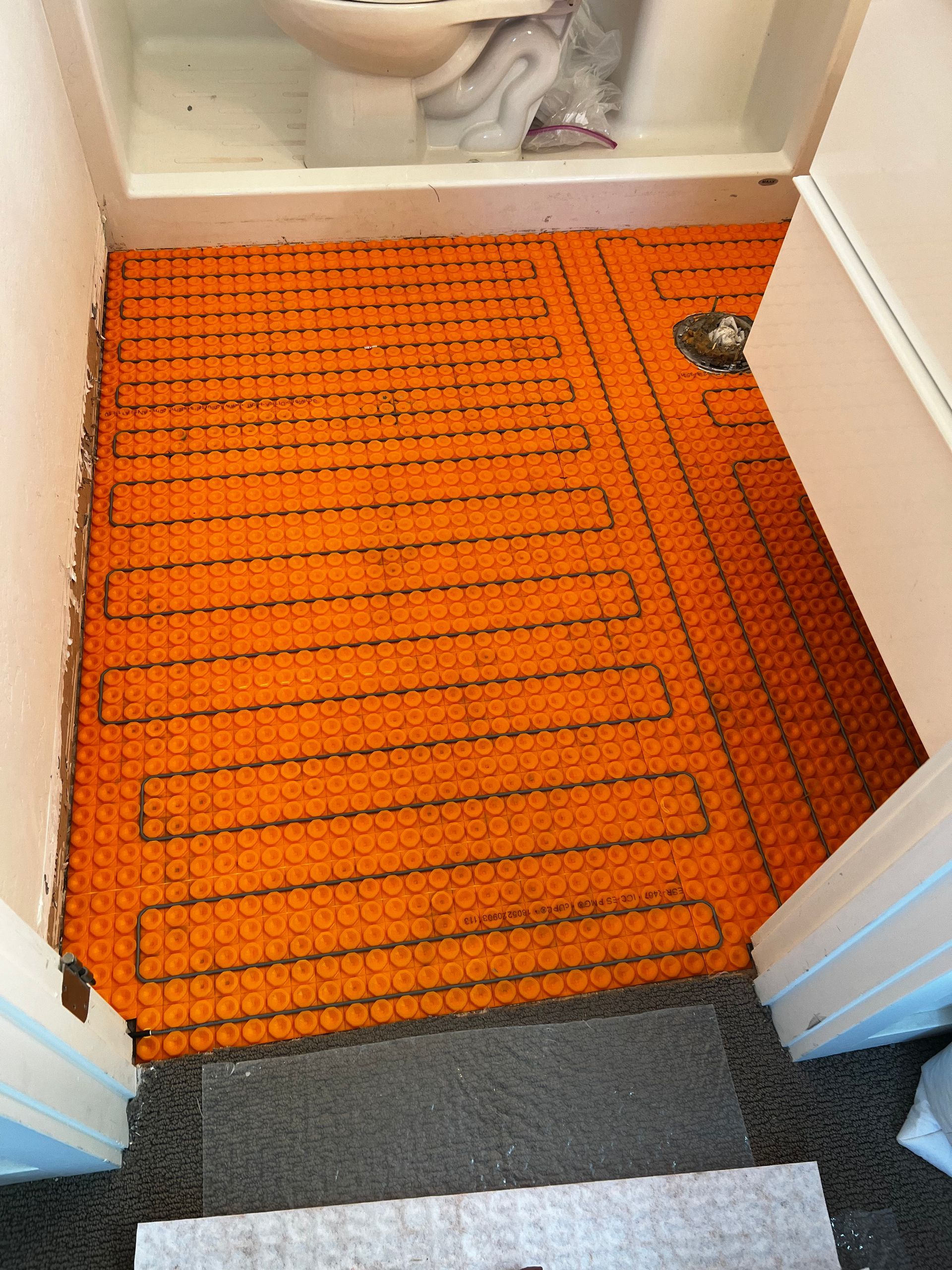 Orange heated floor mat in a doorway between rooms, with gray carpet nearby.