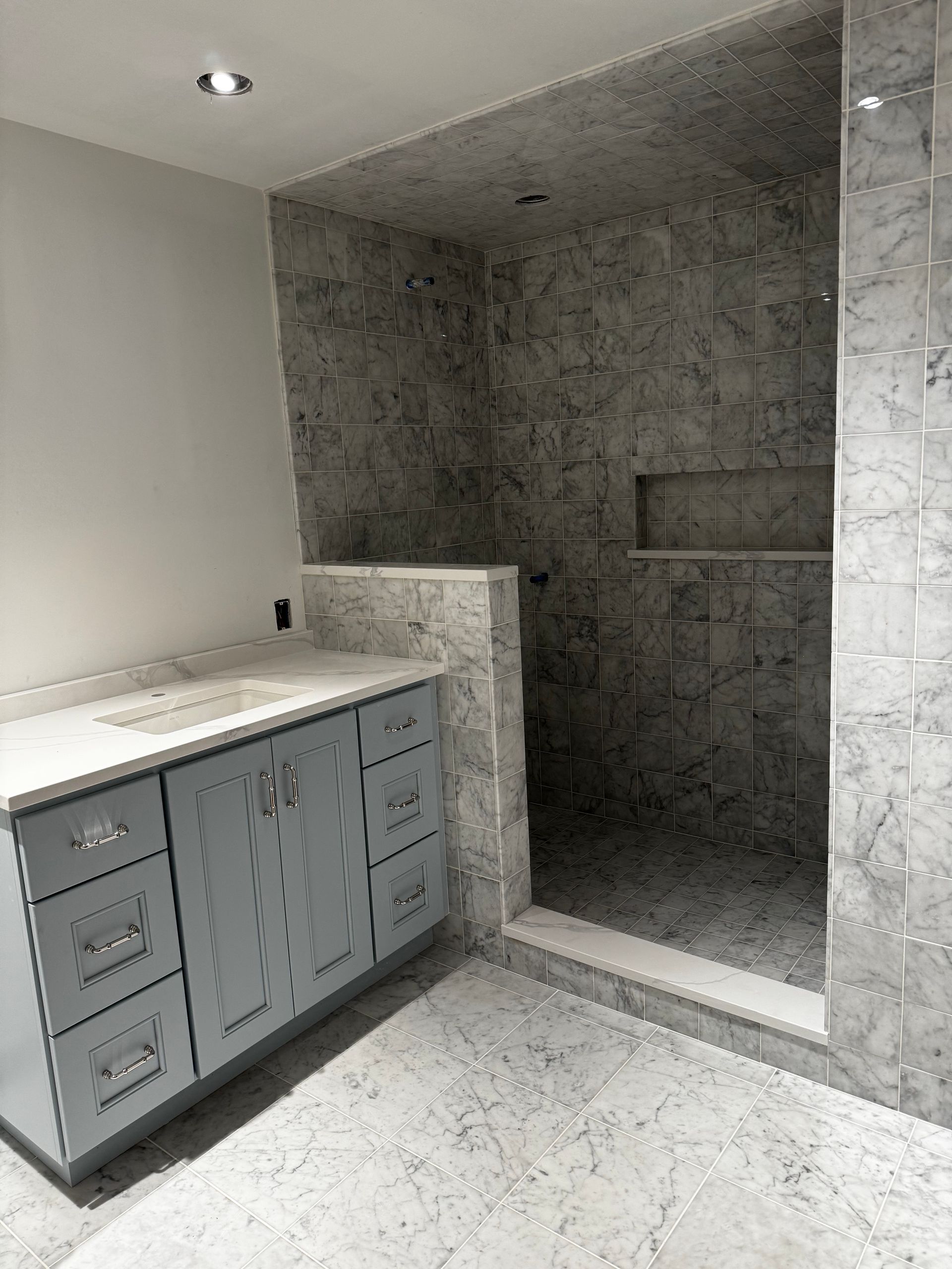Modern bathroom with gray marble shower, white vanity, and tiled floor