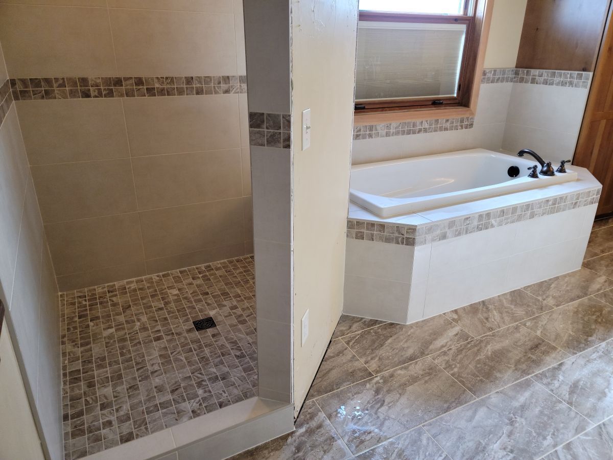 Bathroom with tiled shower on left and corner soaking tub by window on the right