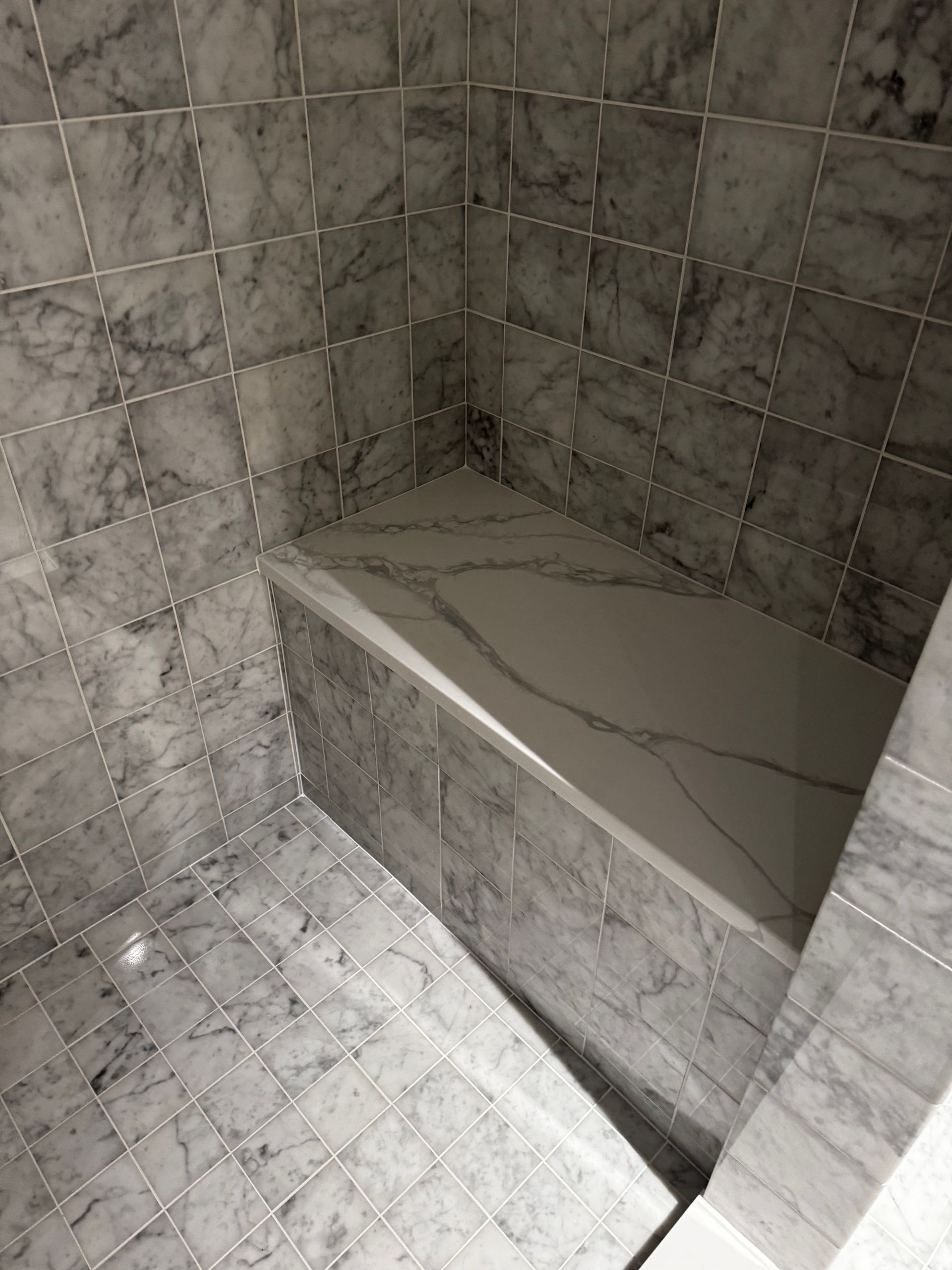 Marble-tiled shower corner with a built-in bench and light gray stone walls