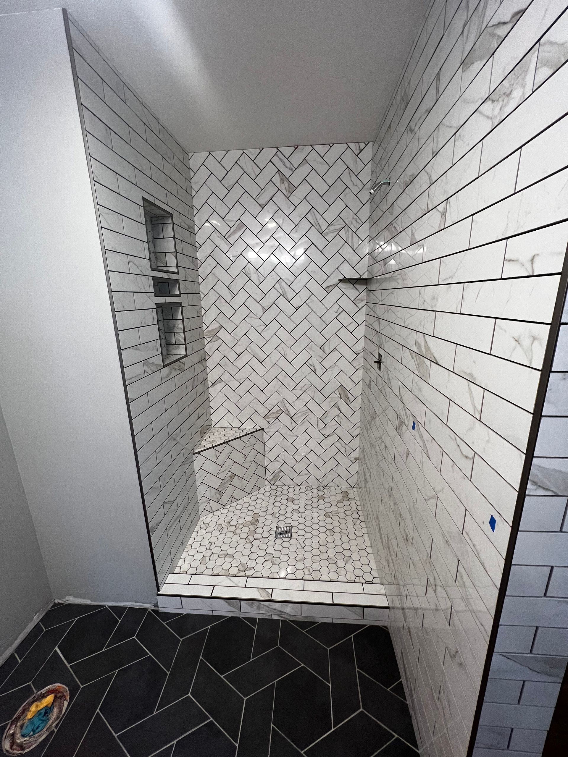 Narrow tiled shower stall with white walls, patterned floor, and built-in shelf niche