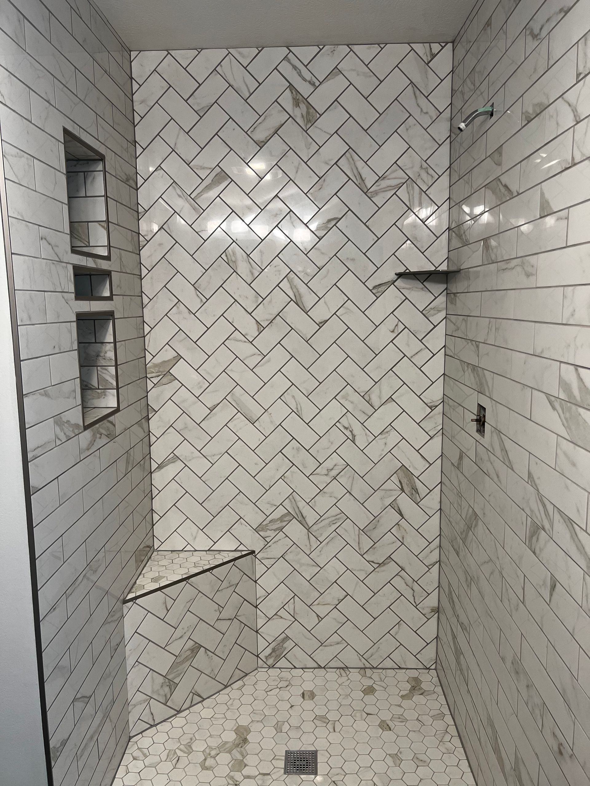 White tiled shower with herringbone pattern, built-in shelves, and a floor drain.
