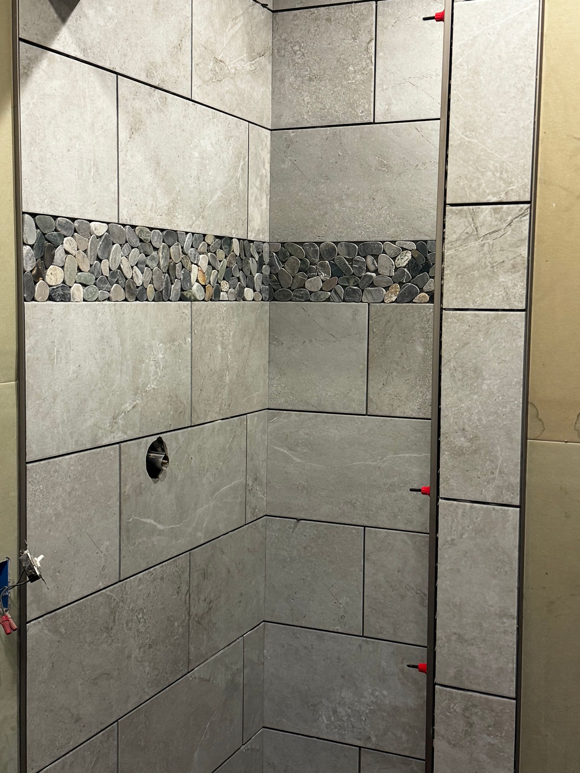 Bathroom shower area with unfinished gray tile walls and a decorative mosaic accent strip