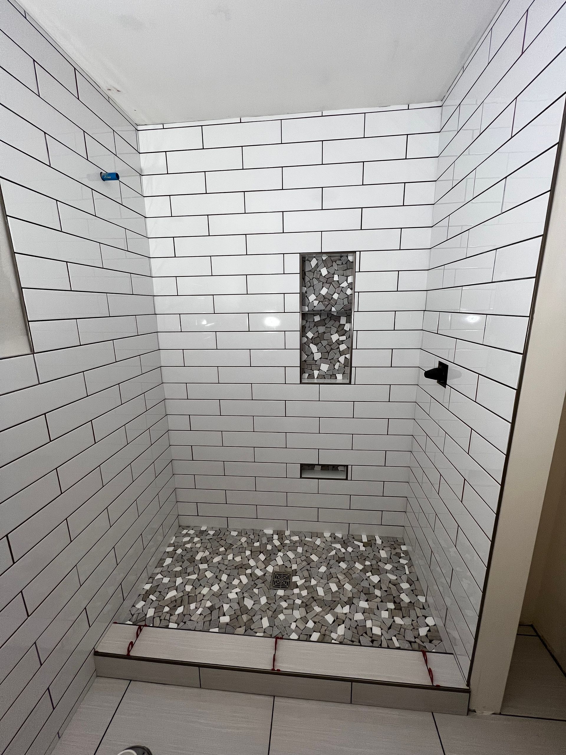 Empty tiled shower stall with a pebble-floor drain and a small wall niche.