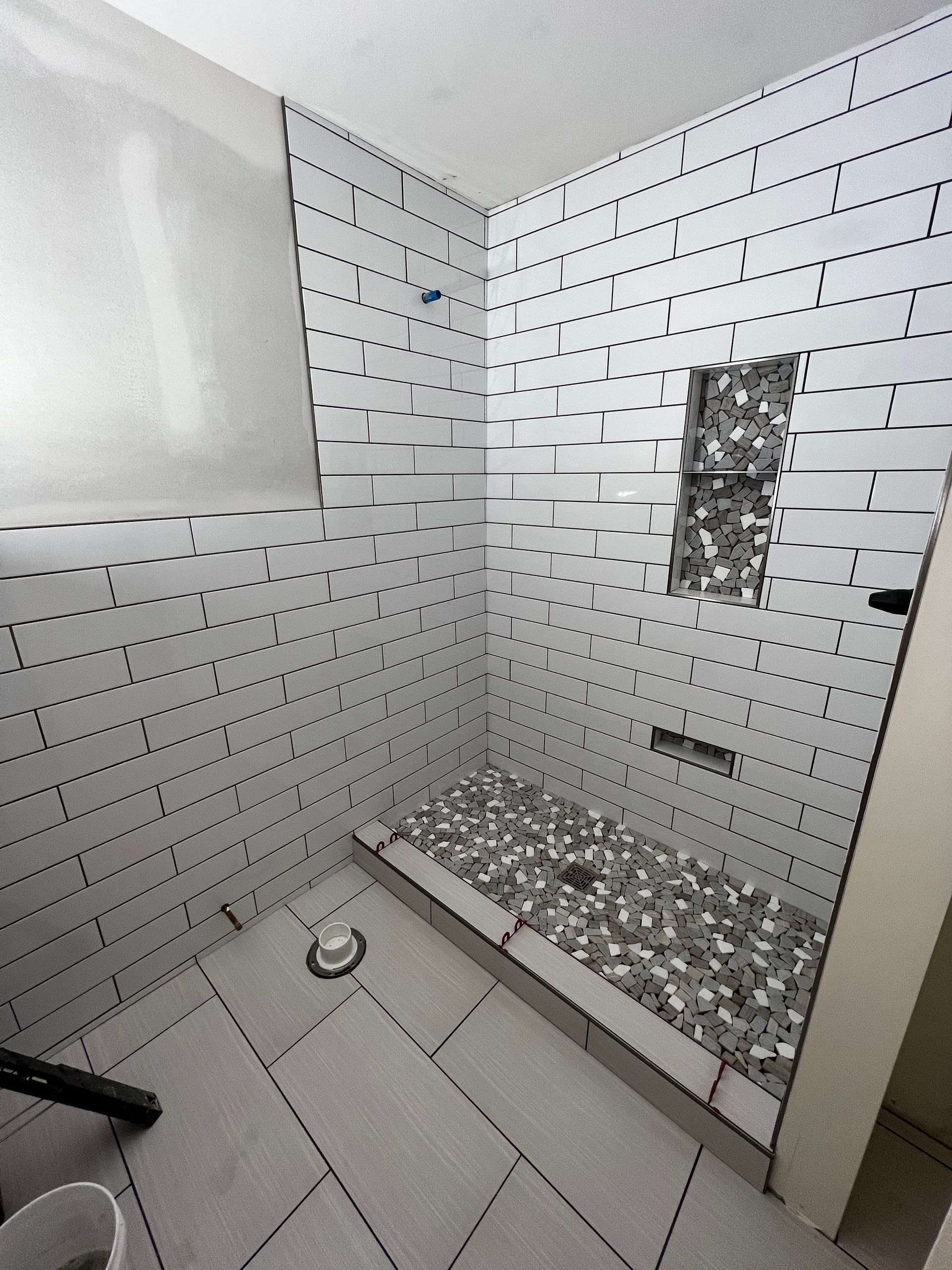 Small tiled shower stall with a built-in bench, white walls, and a small recessed niche.