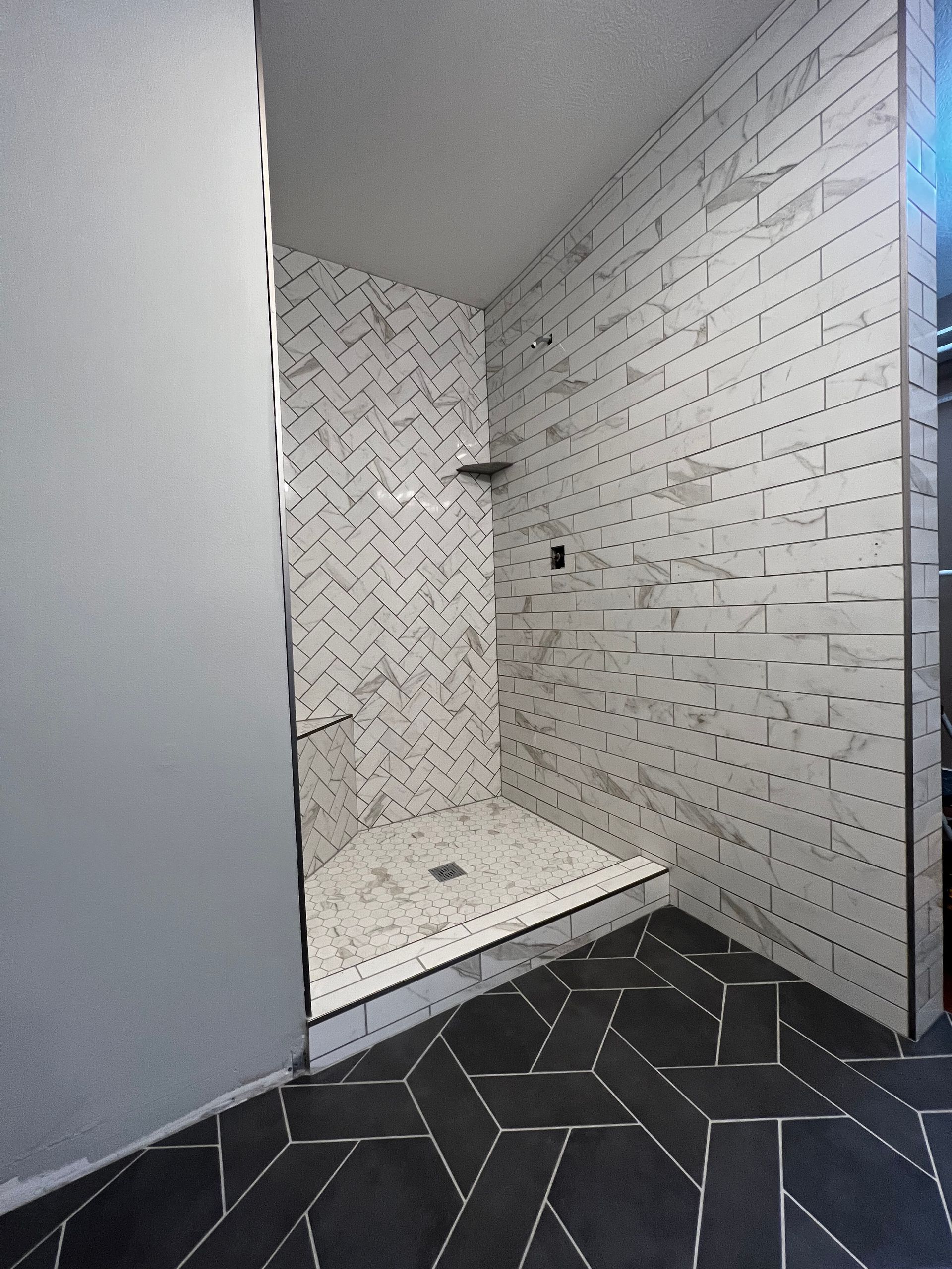 Empty tiled shower stall with black floor tiles and white patterned wall tiles.