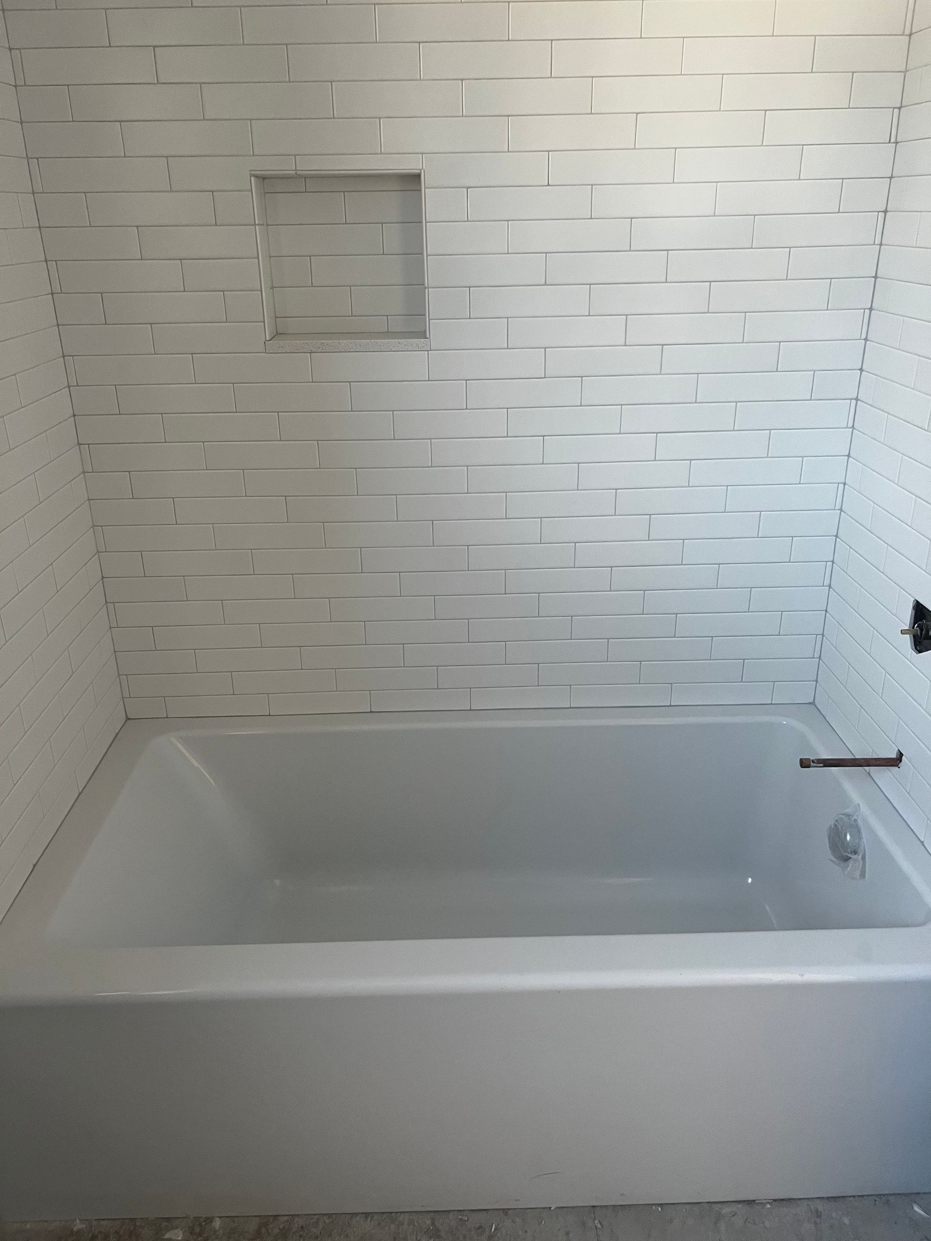 White bathtub in a tiled bathroom with a built-in niche and shower fixtures