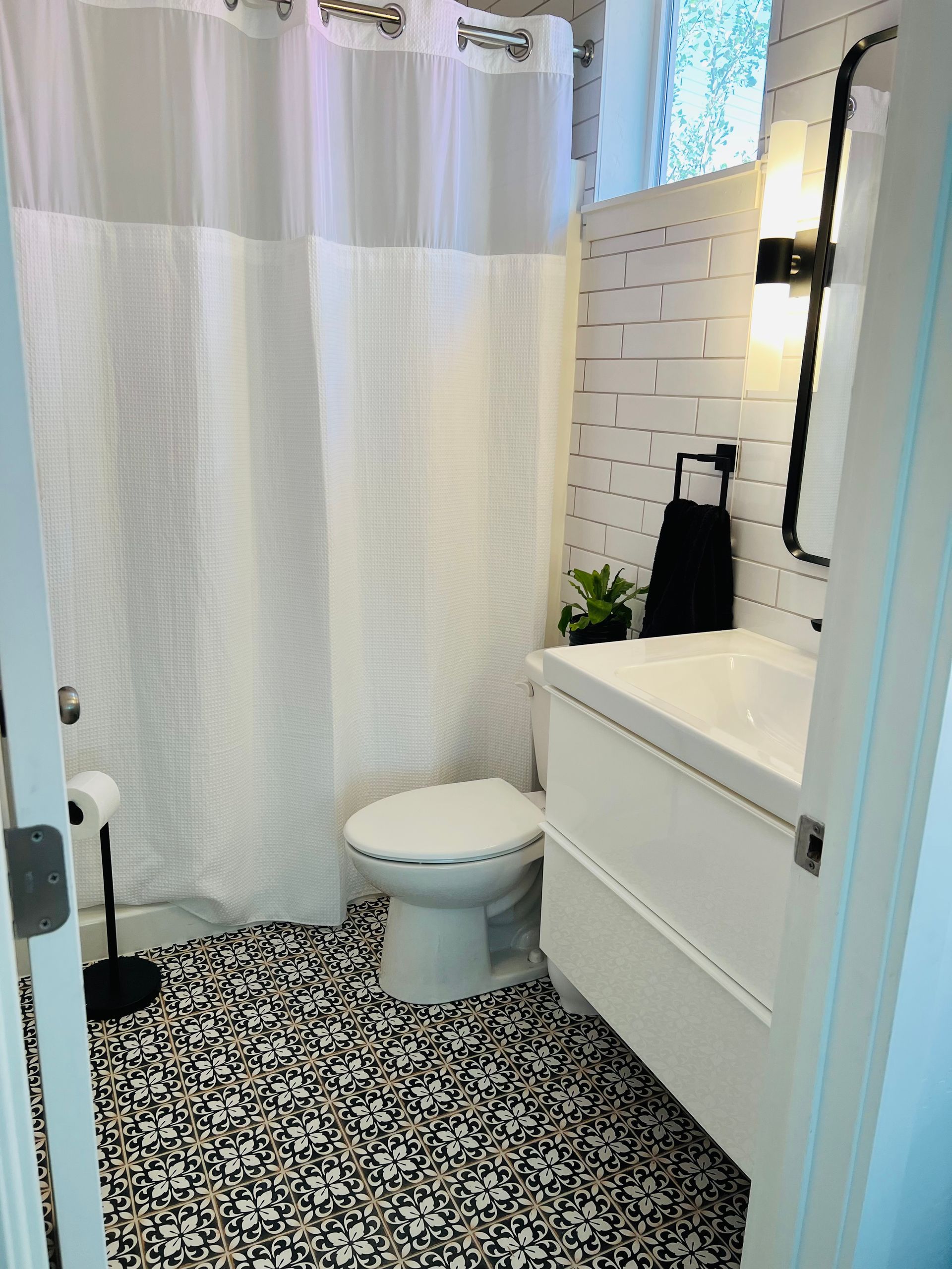Small bathroom with black-and-white patterned floor, shower curtain, toilet, and vanity sink.