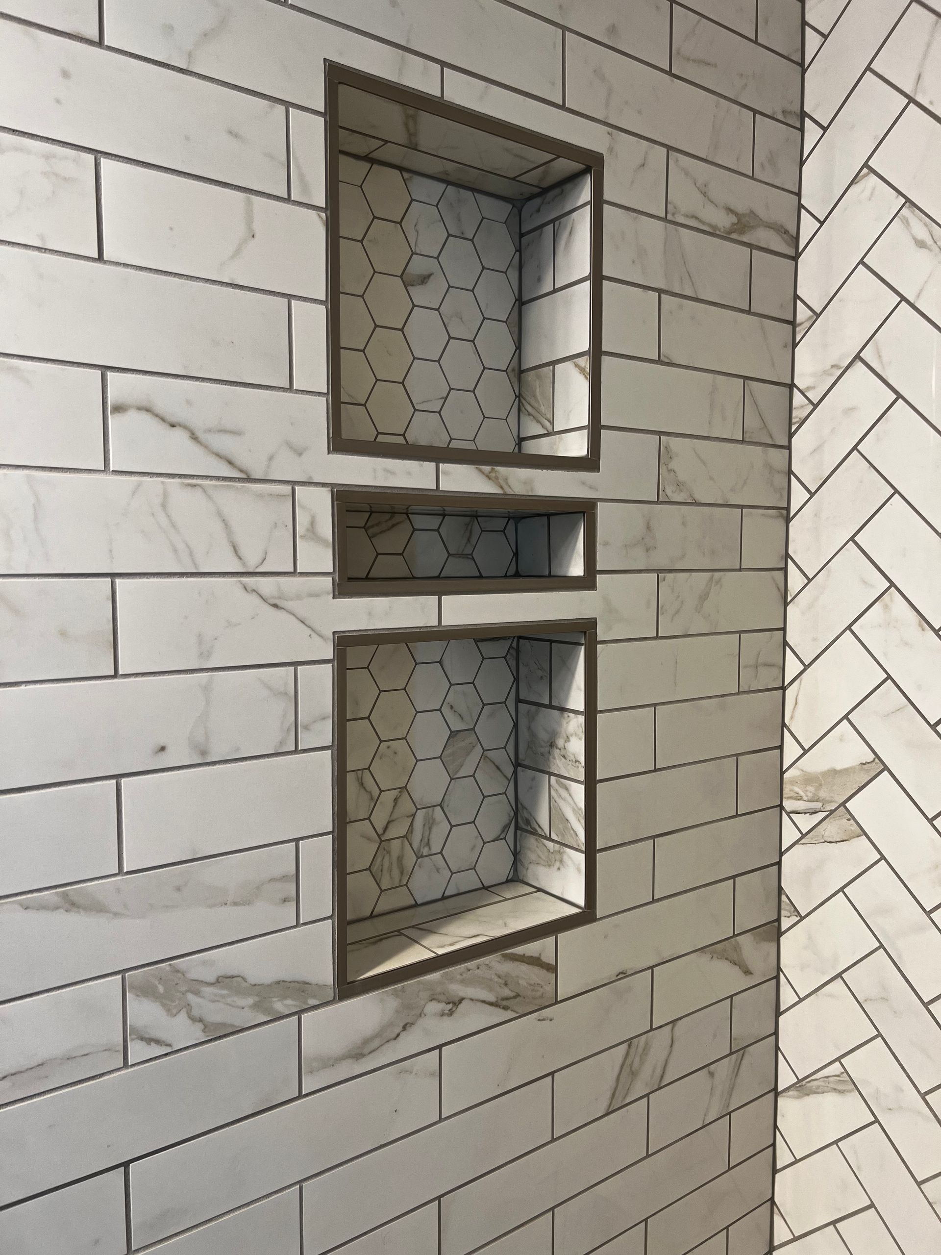 Narrow wall niche with three small frosted glass windows set in light marble tiles.