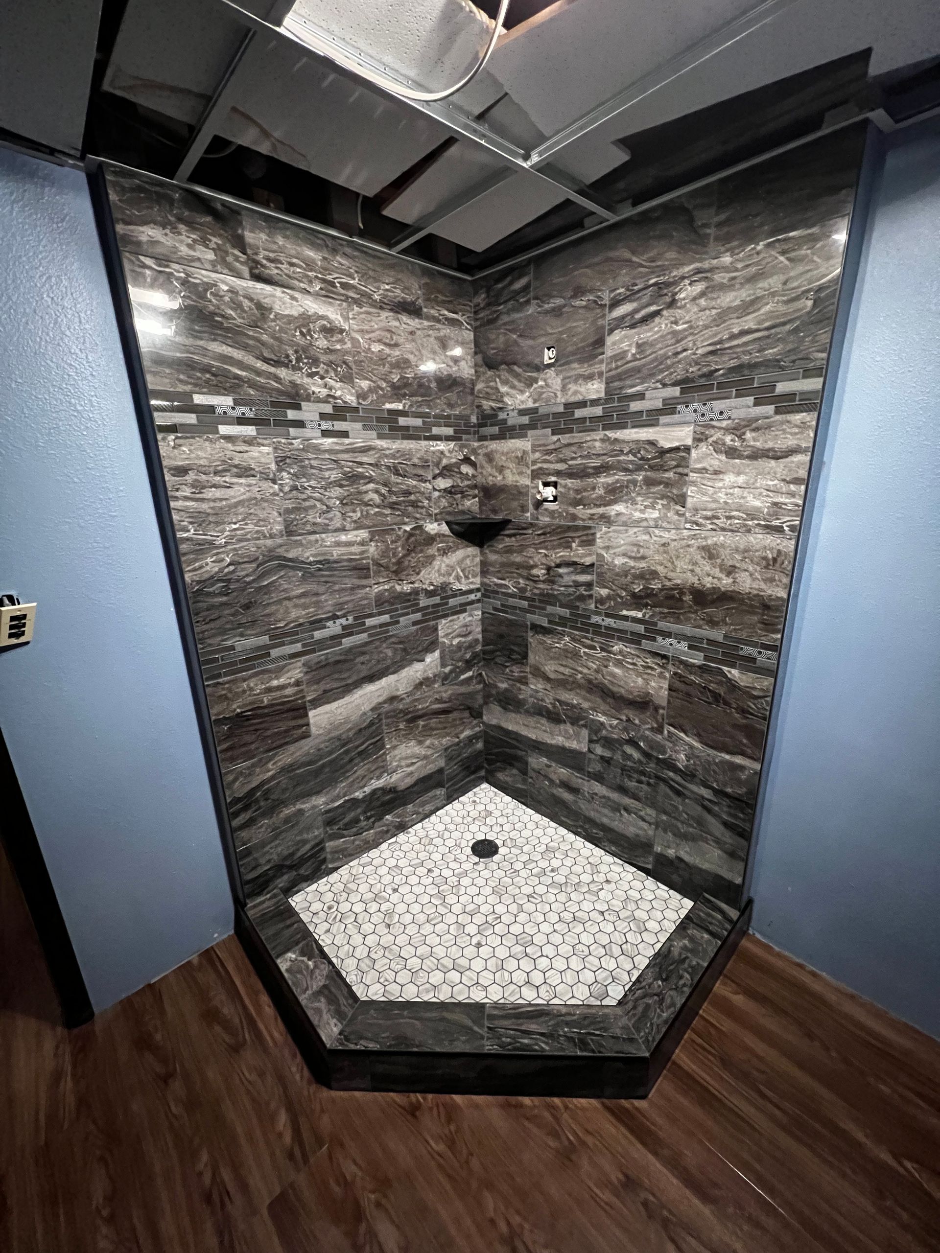 Corner shower with dark stone tile walls, white mosaic floor, and a black shower head in a bathroom.