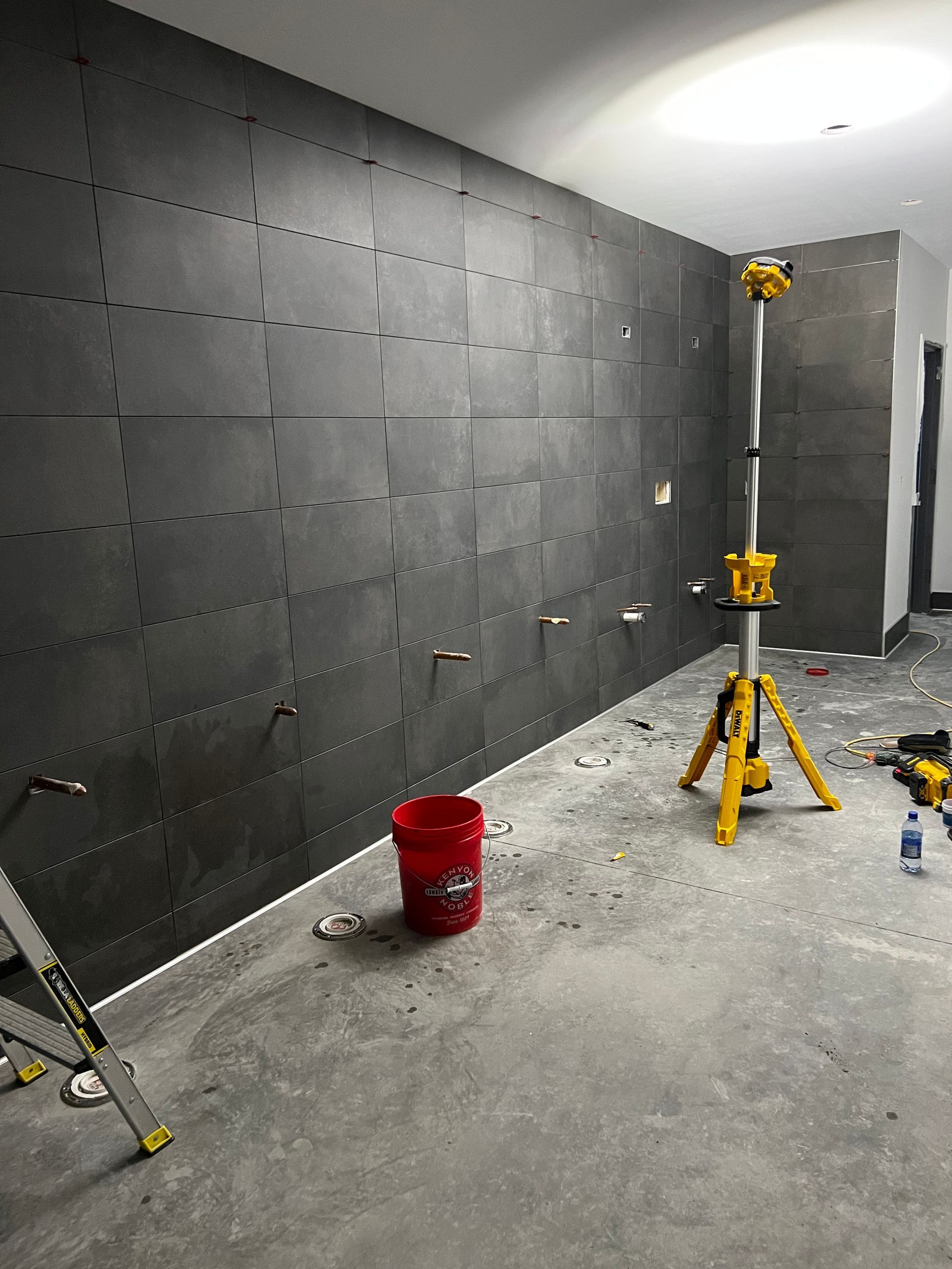 Partially finished room with black acoustic panels, concrete floor, and construction tools, including a red bucket and yellow tripod