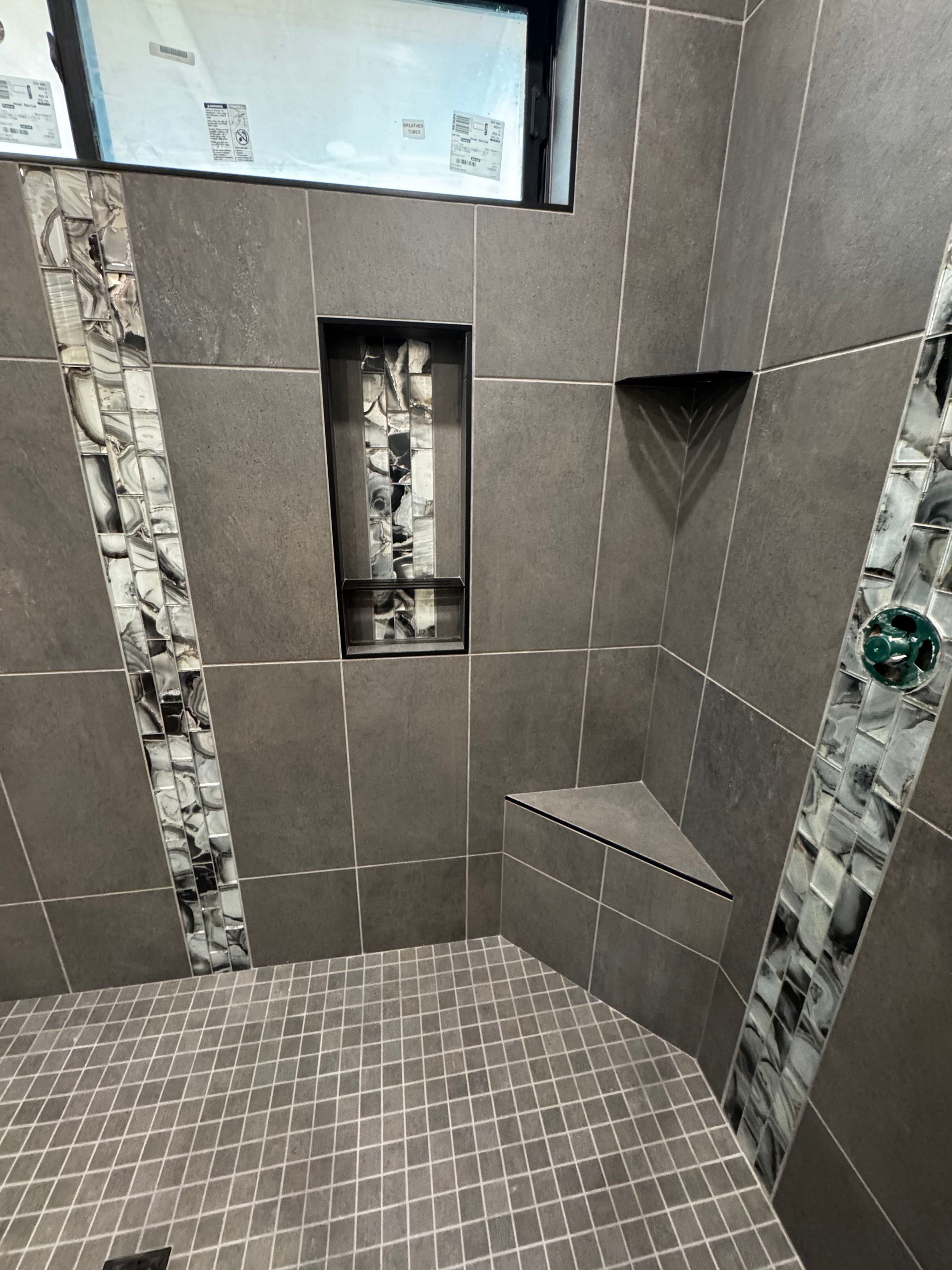 Tiled shower stall with recessed shelves and a glass soap holder, in gray and brown tones