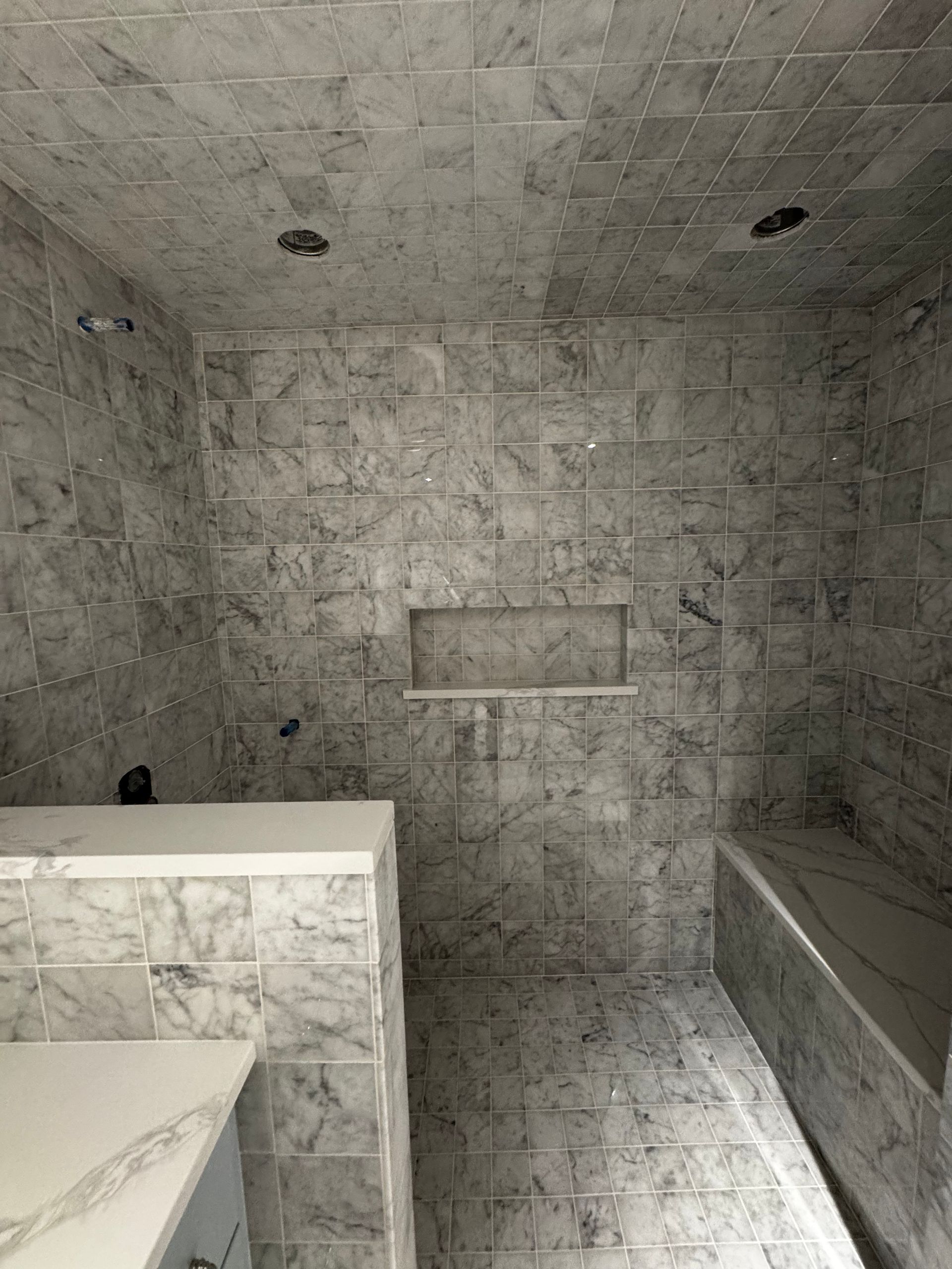 Gray tiled bathroom with a white sink vanity and a built-in bench or tub on the right