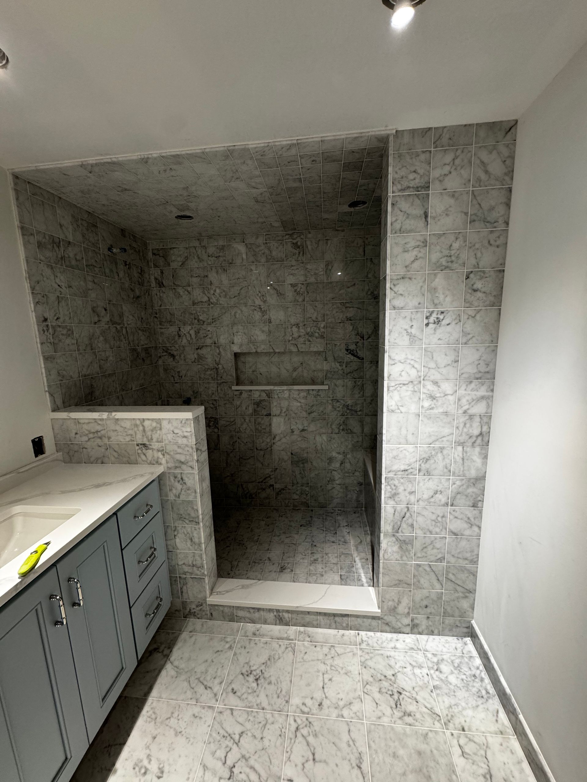 Empty bathroom with gray tiled walk-in shower and vanity cabinets in progress