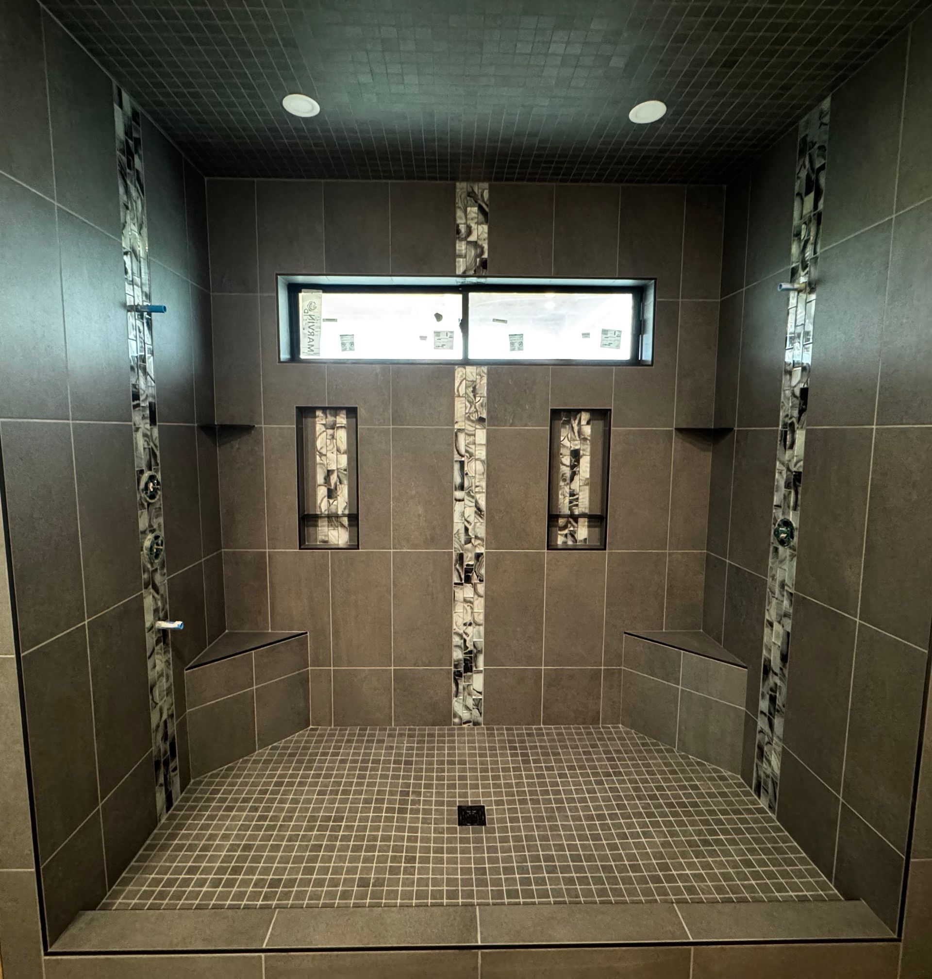 Modern tiled walk-in shower with a bench, dual shower fixtures, and high windows.