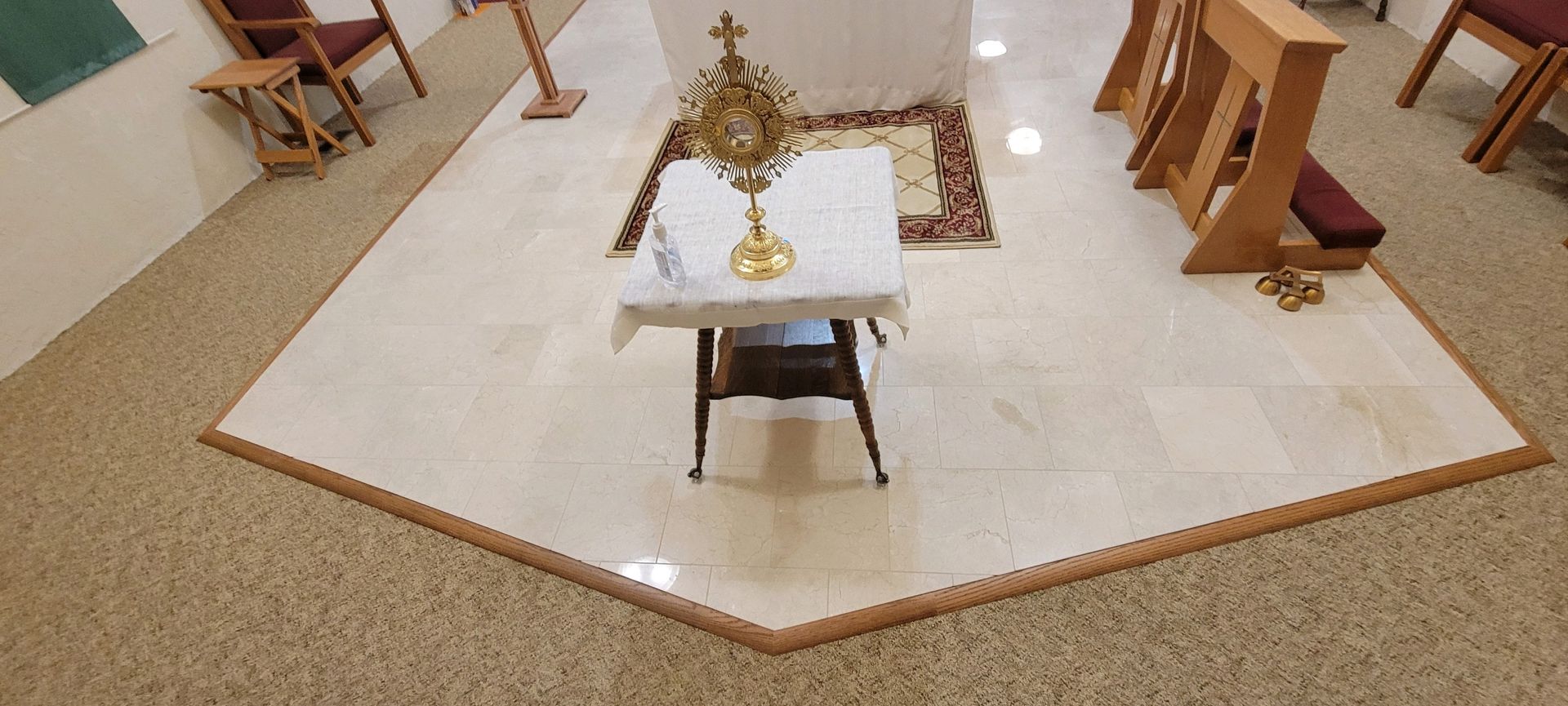 Church altar on a white platform with candles, a central table, and wooden chairs around it.