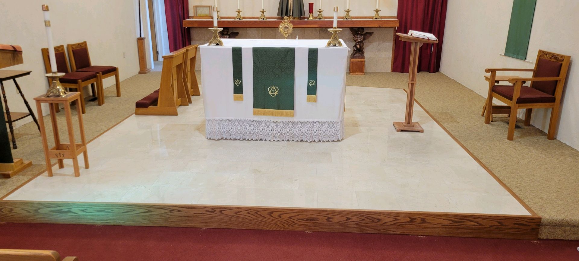 Church altar with white cloth, green liturgical banner, candles, chairs, and red curtains in a sanctuary