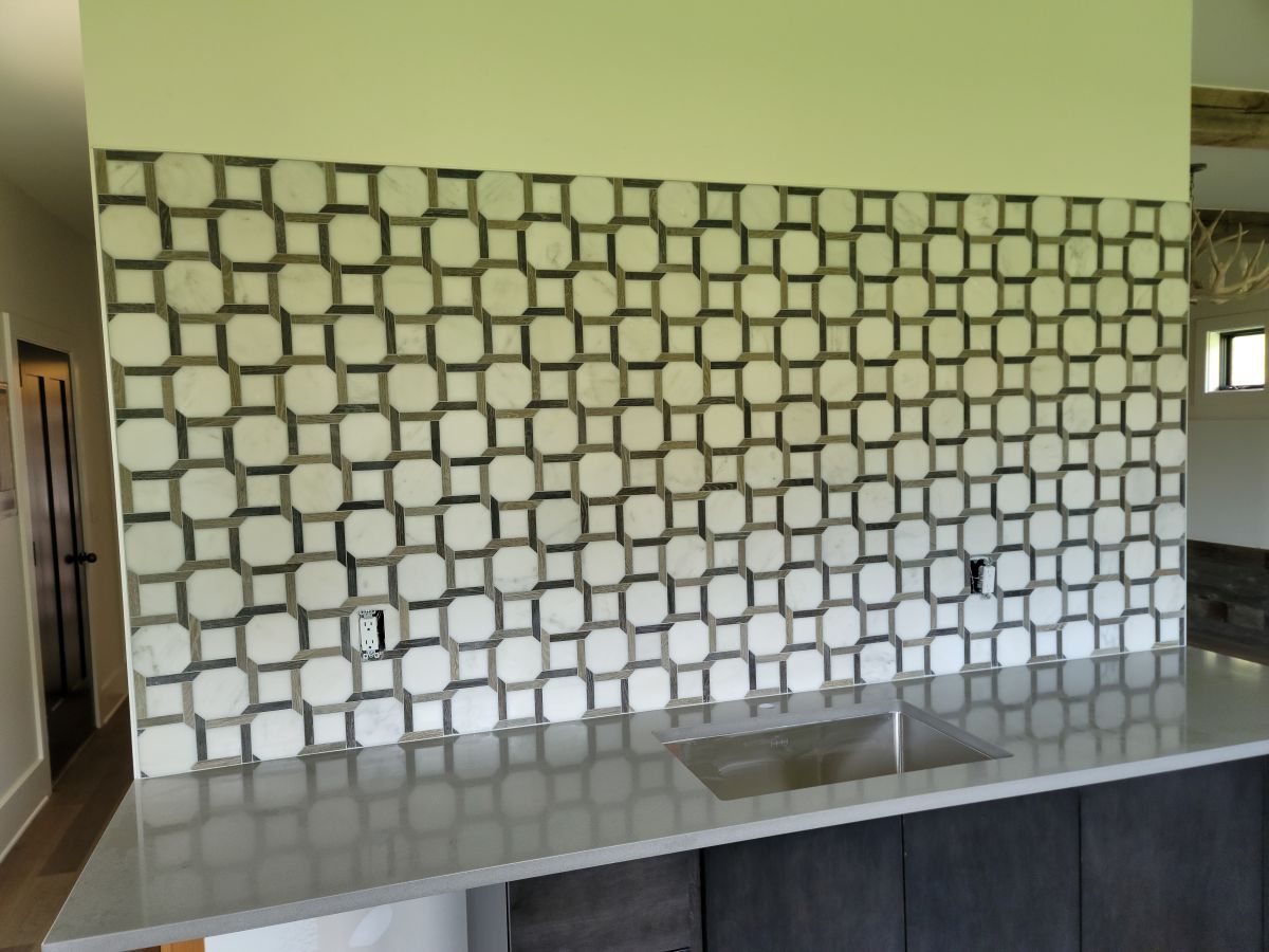 Kitchen counter with geometric tile backsplash and stainless sink under a green wall.