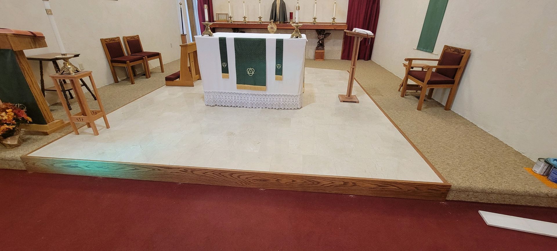 Empty church altar with white cloth, candles, chairs, and red carpet in a small sanctuary