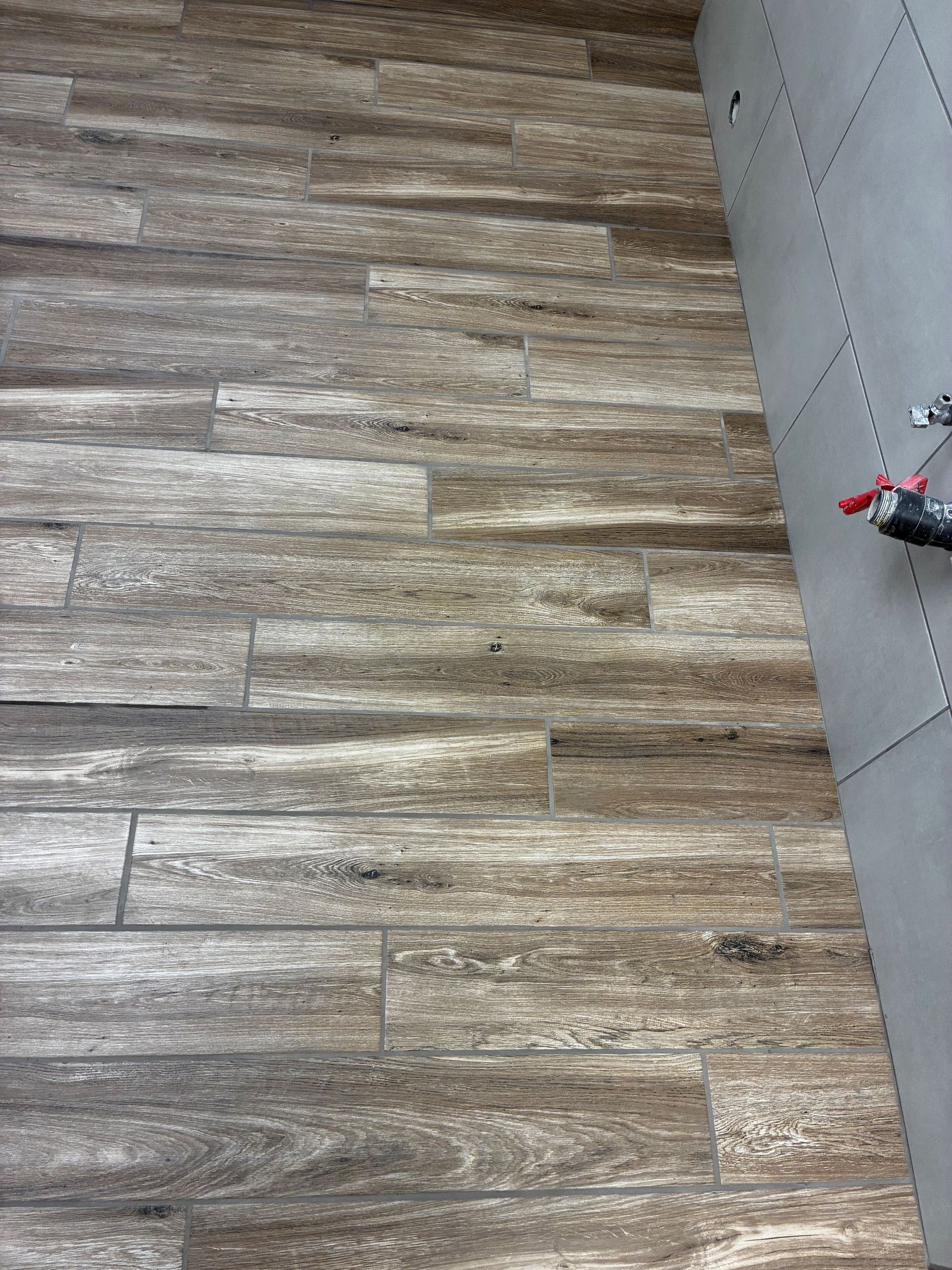 Wood-look tile floor beside a light gray wall with a small red object at the edge