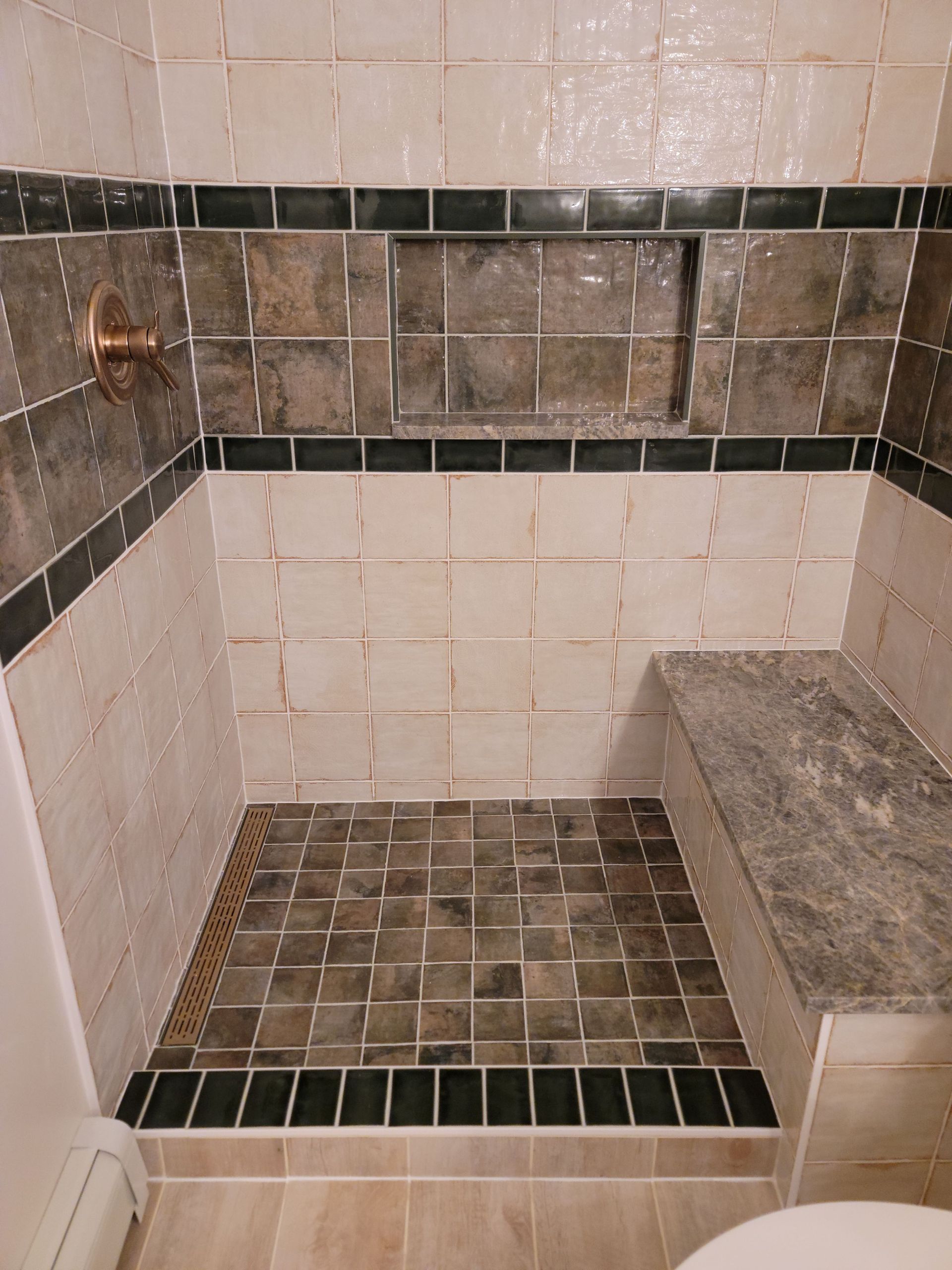Tiled walk-in shower with bench, copper showerhead, and dark mosaic accents