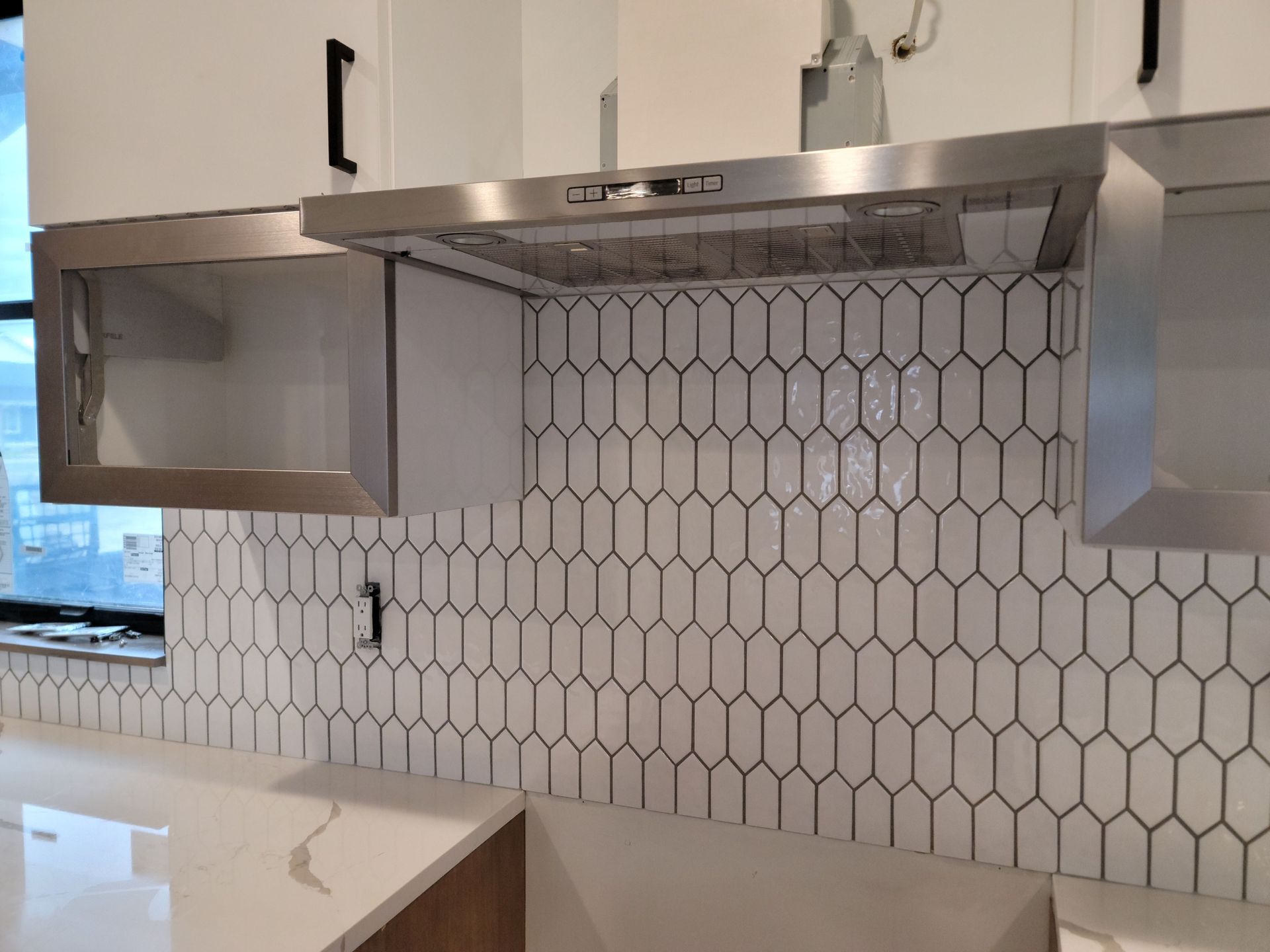 Modern kitchen with stainless steel range hood and white hexagon tile backsplash