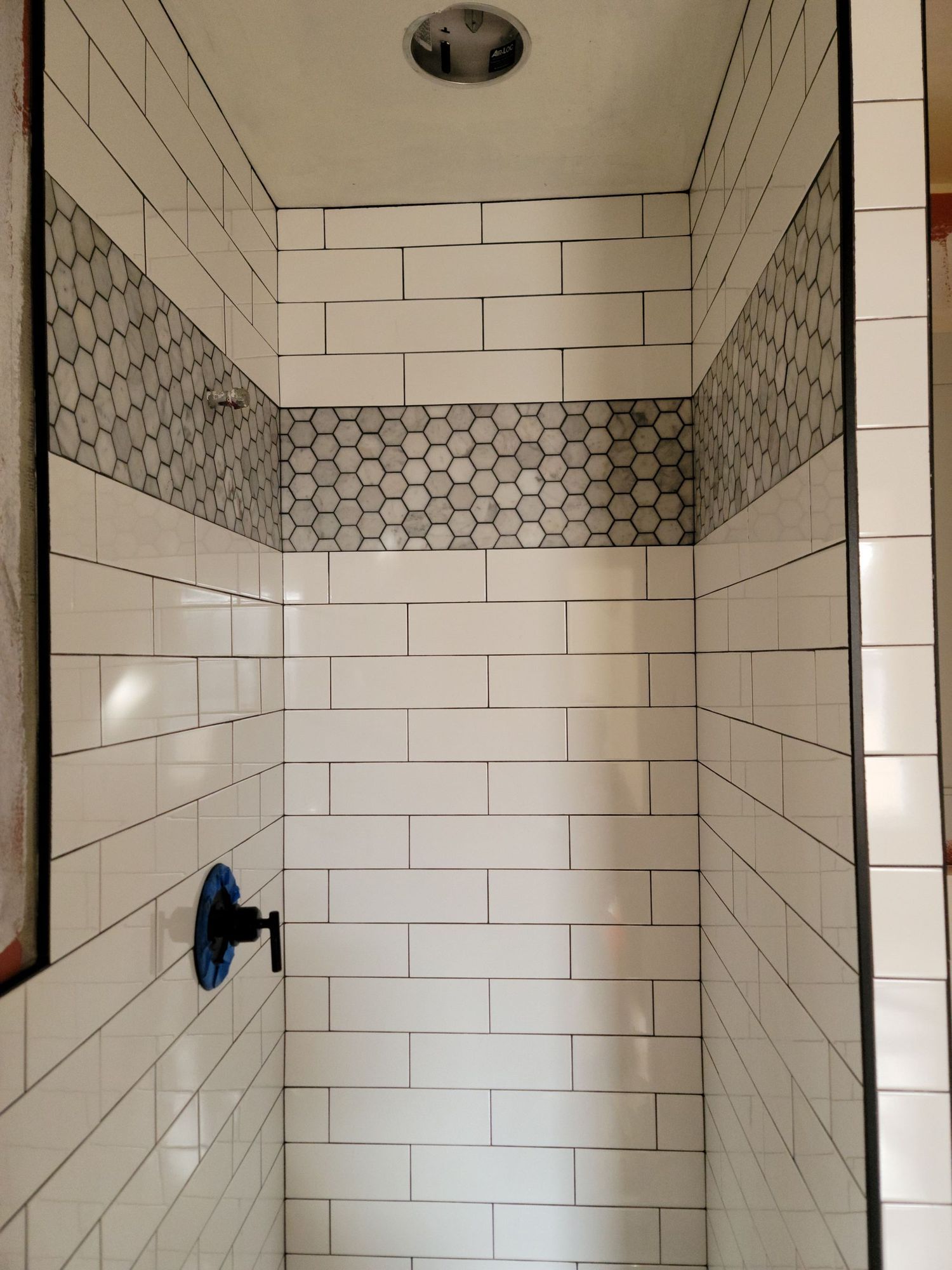Tiled shower stall with white subway tiles, gray accent band, and a blue shower valve handle