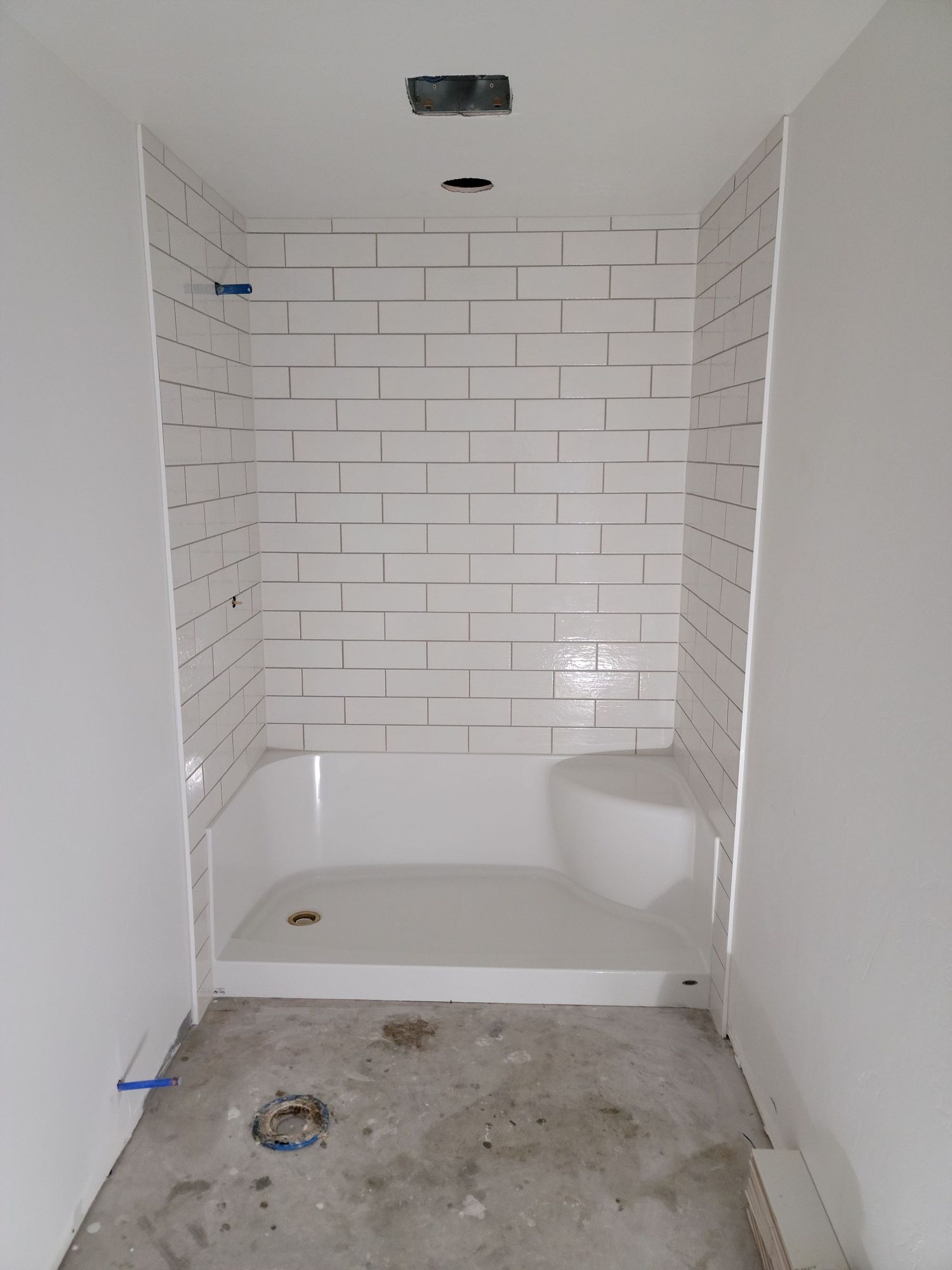 Empty shower under construction with white subway tile walls and a bare concrete floor.