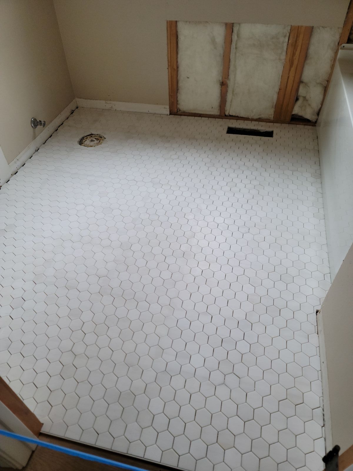 Small unfinished bathroom with white hex tile floor, exposed wall studs, and a drain.