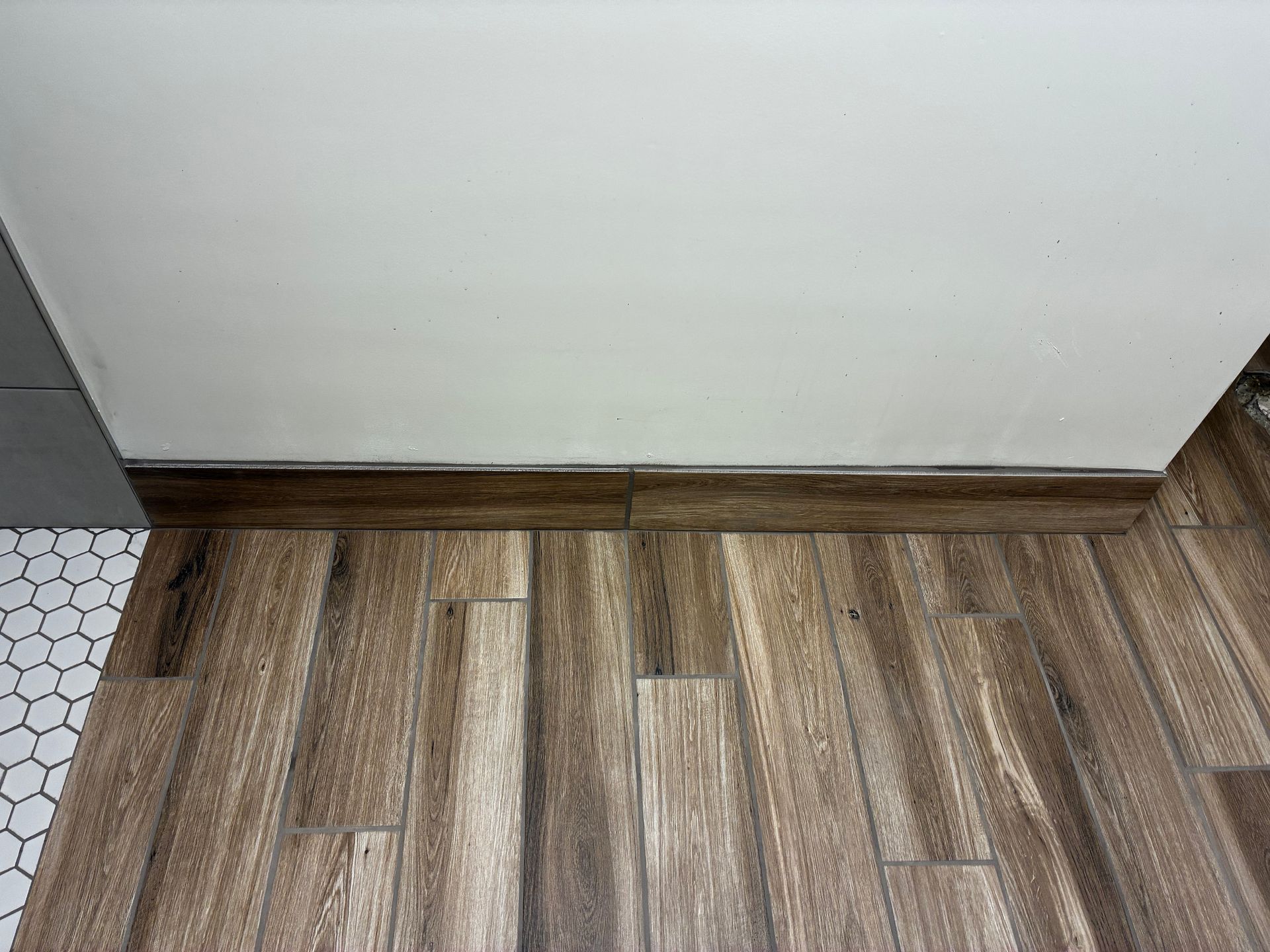 Wood-look vinyl floor meeting a white wall with dark baseboard trim.