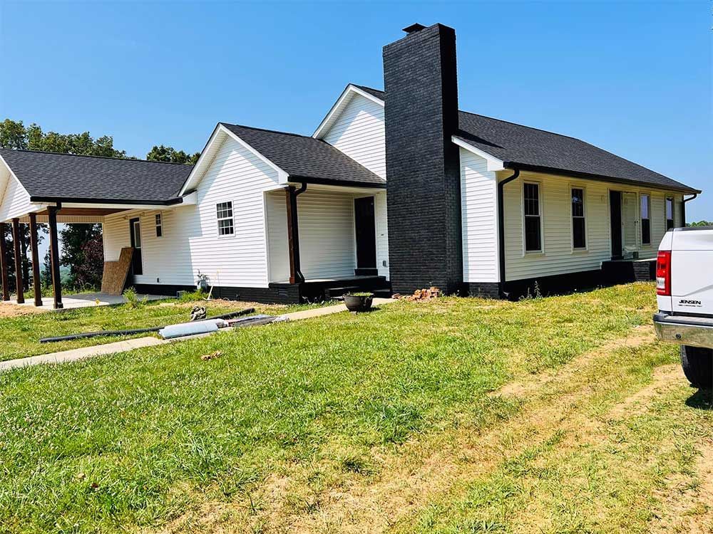 A white truck is parked in front of a white house with a black chimney.