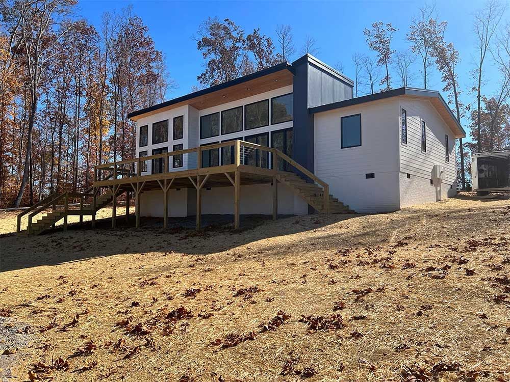 A white house with a large deck is sitting on top of a dirt hill.