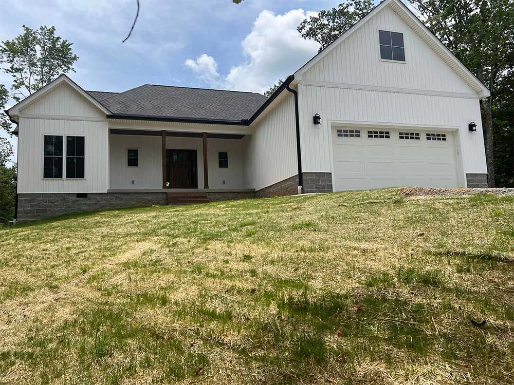 A white house with a garage is sitting on top of a grassy hill.