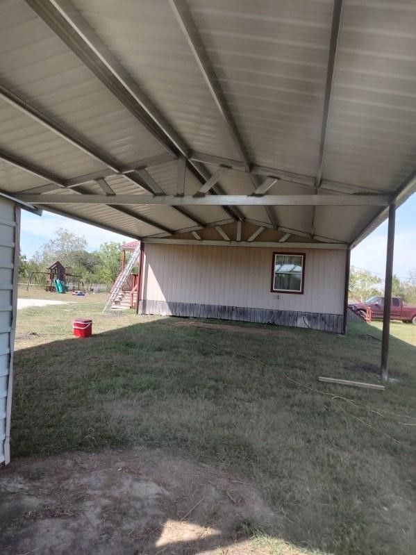 A covered parking lot with a house in the background.