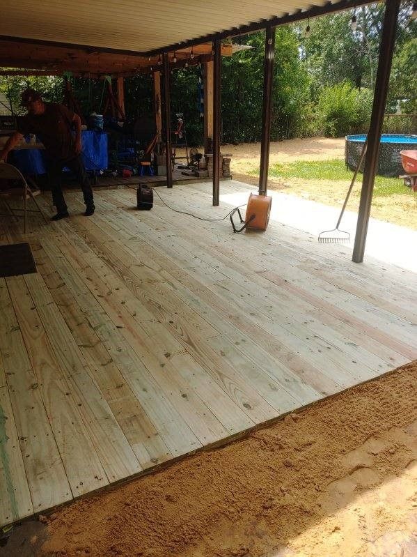 A man is standing on a wooden deck under a canopy.