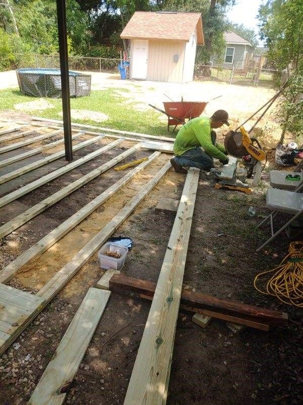 A man is kneeling down on a wooden deck under construction.