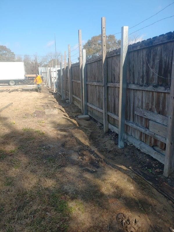 A wooden fence is being built next to a dirt road.