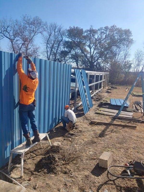 Two men are working on a blue metal fence.