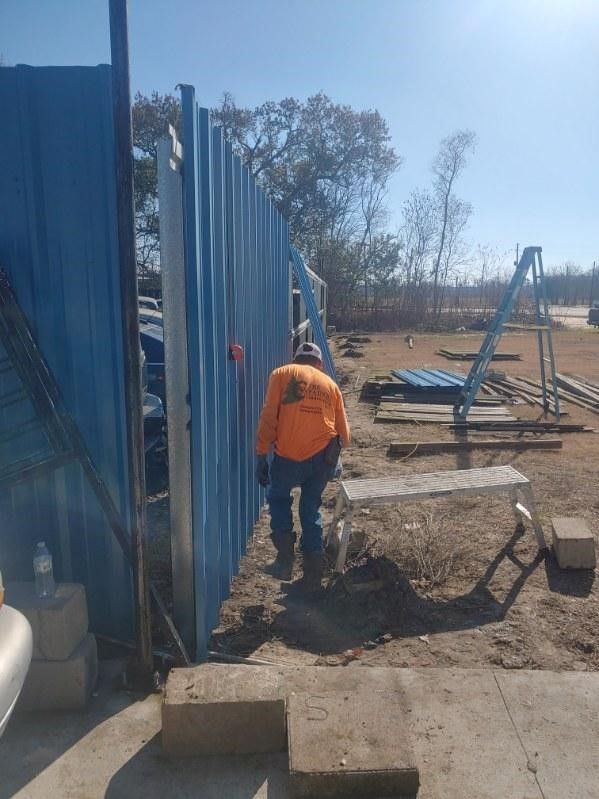A man in an orange shirt is standing next to a blue fence.