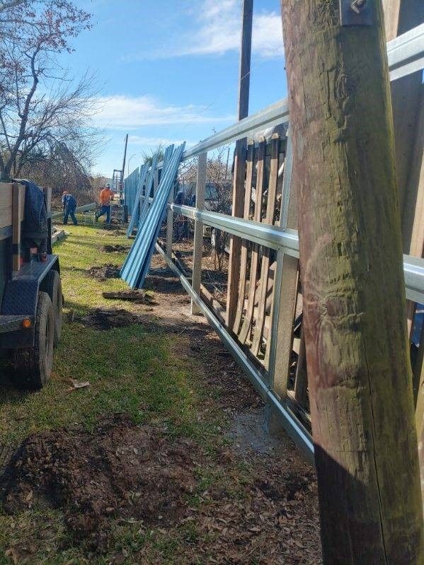 A trailer is parked in the grass next to a wooden fence.