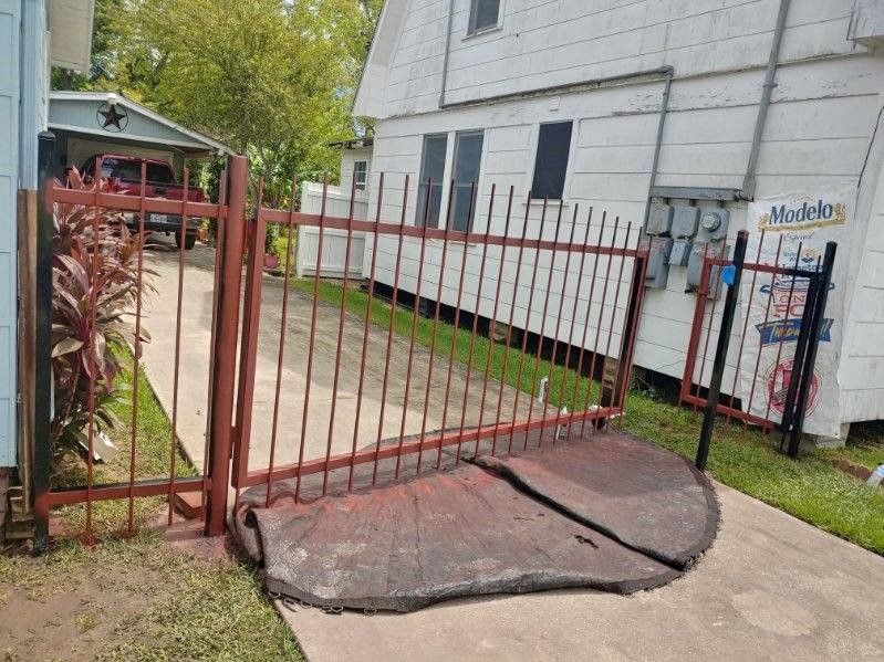 A red fence is broken in front of a white house.