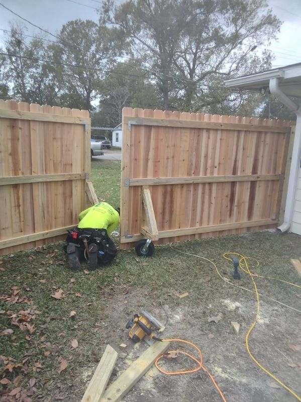 A man is working on a wooden fence in a backyard.