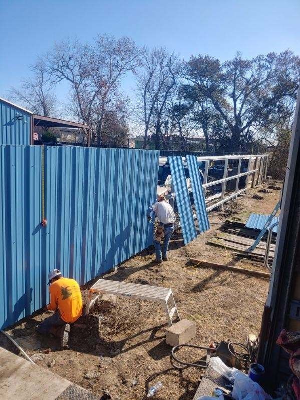 Two men are working on a blue metal fence.