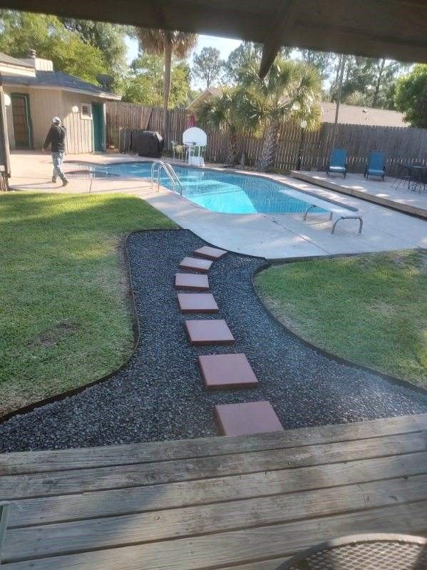 A man is walking towards a swimming pool in a backyard.