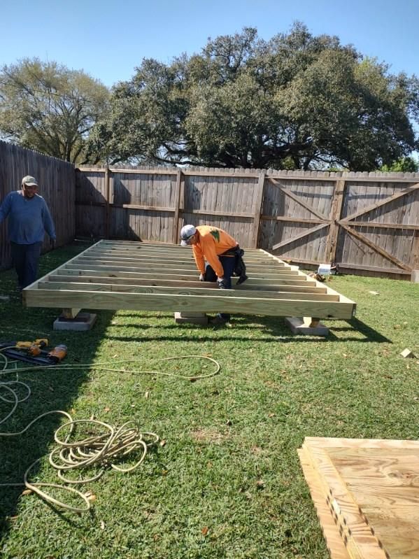 A man is working on a wooden deck in a backyard.