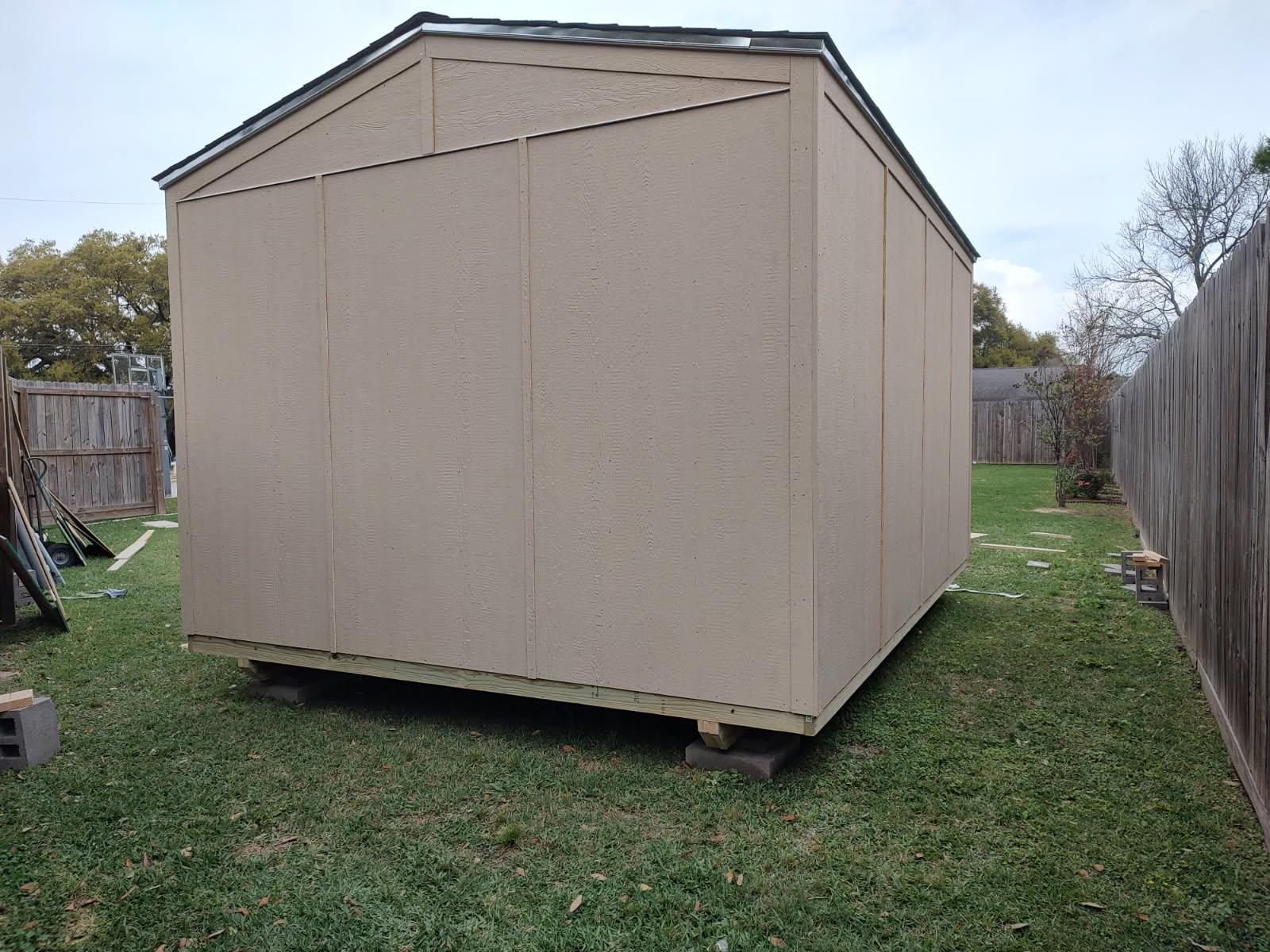 A shed is sitting in the grass next to a fence.