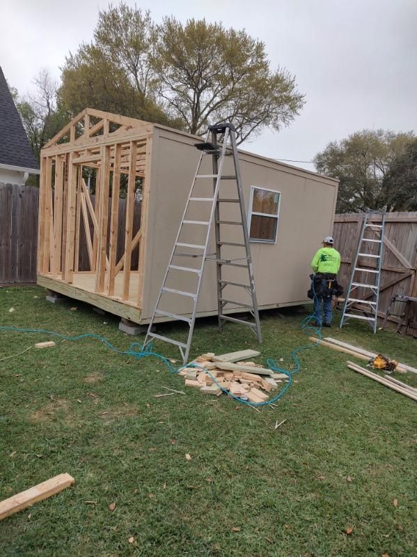 A man is standing next to a ladder in front of a shed being built.