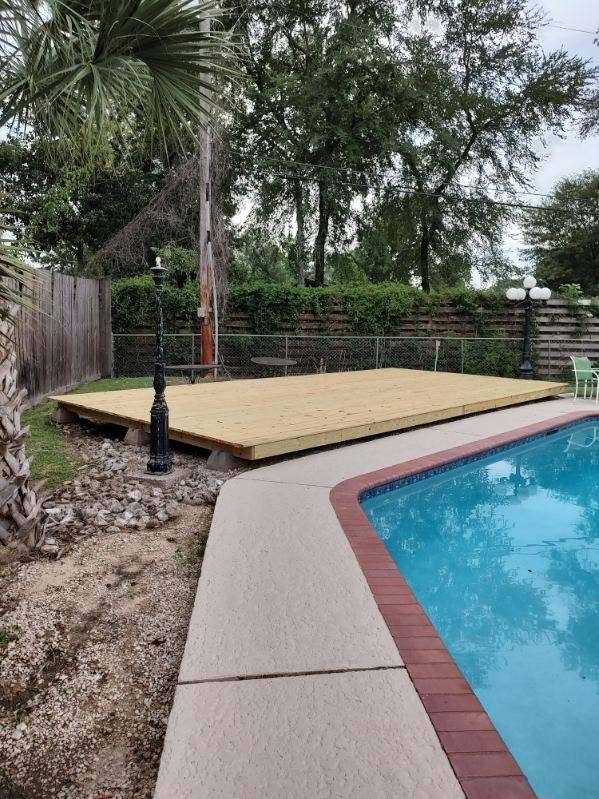 A wooden deck is sitting next to a swimming pool.