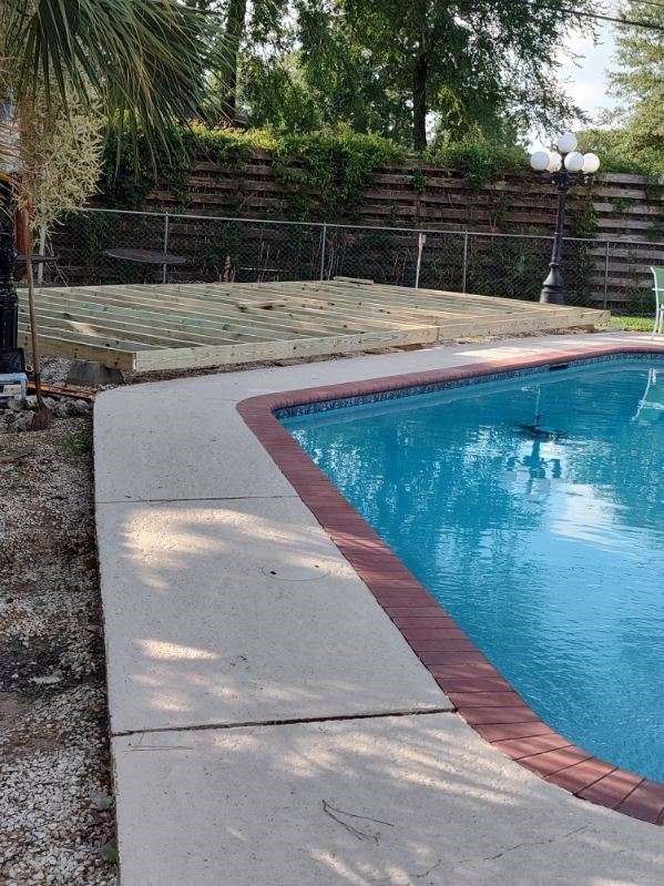 A large swimming pool with a brick border and a wooden fence in the background.